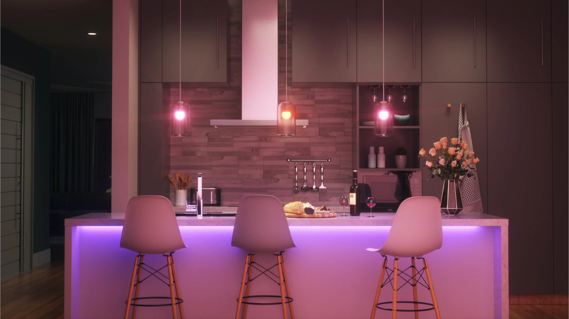Cucina moderna con bancone, tre sedie, fiori e illuminazione.