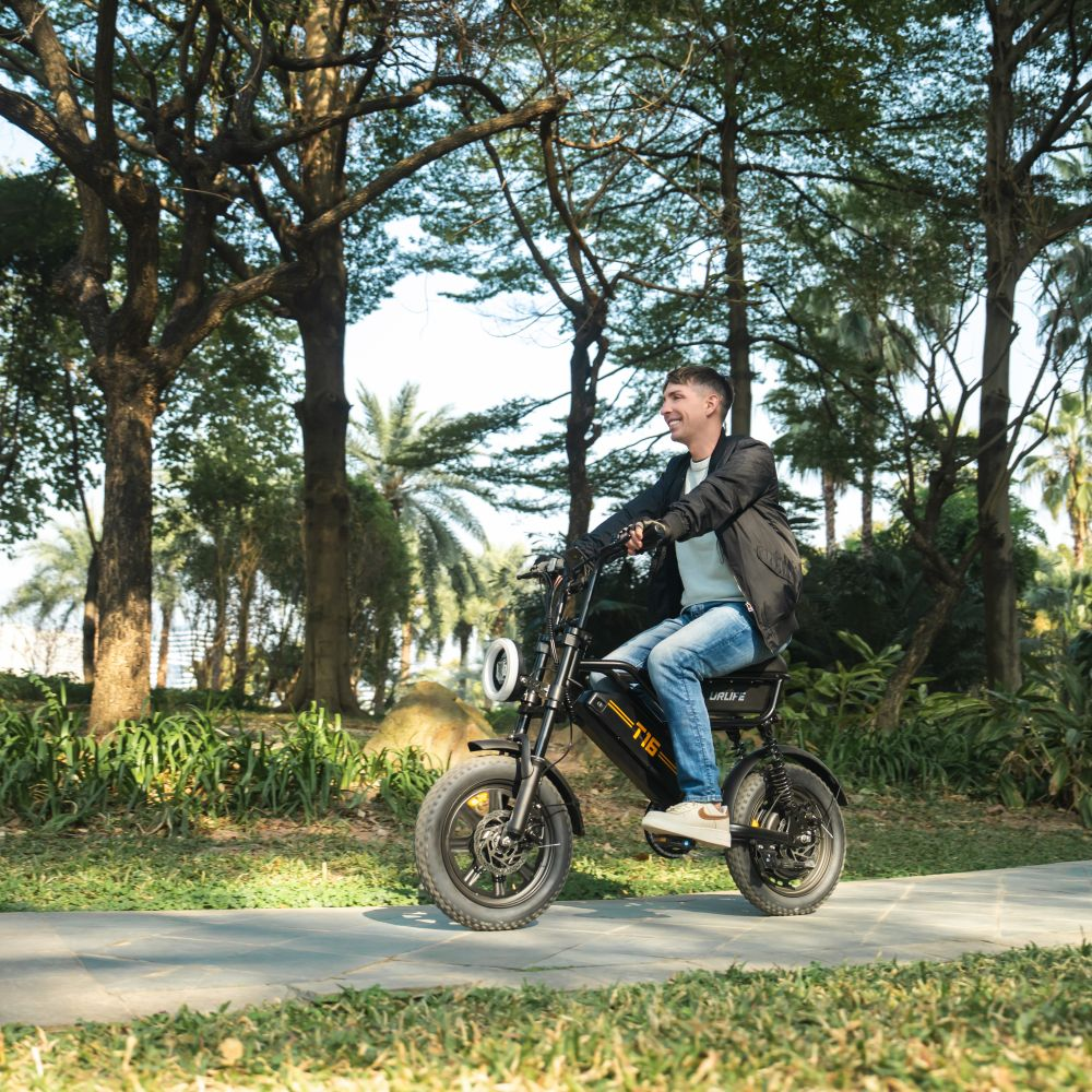 Un uomo guida una bici elettrica nera su un sentiero nel parco, tra gli alberi.