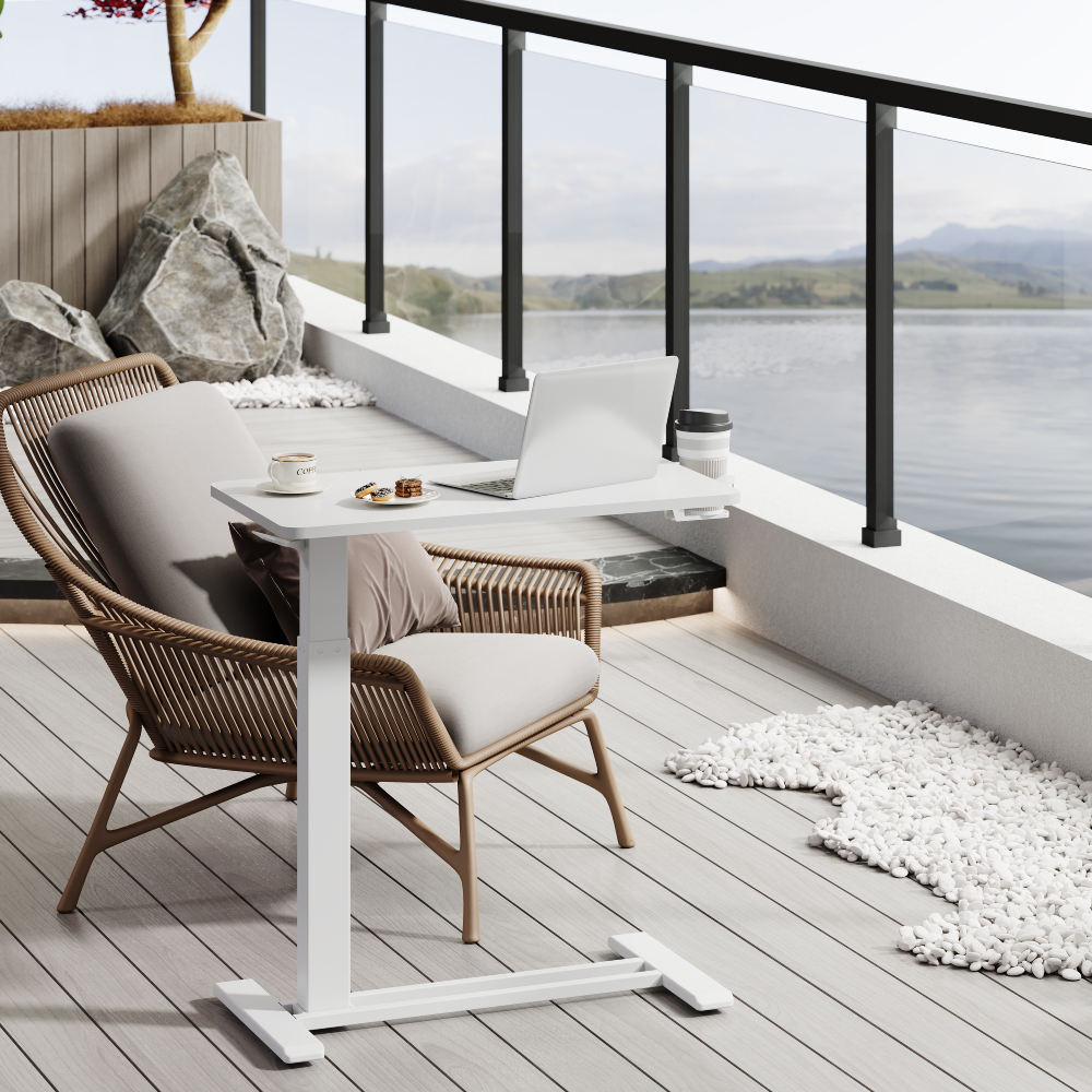 Une table réglable blanche avec ordinateur portable, café et pâtisseries est sur un balcon donnant sur un lac.