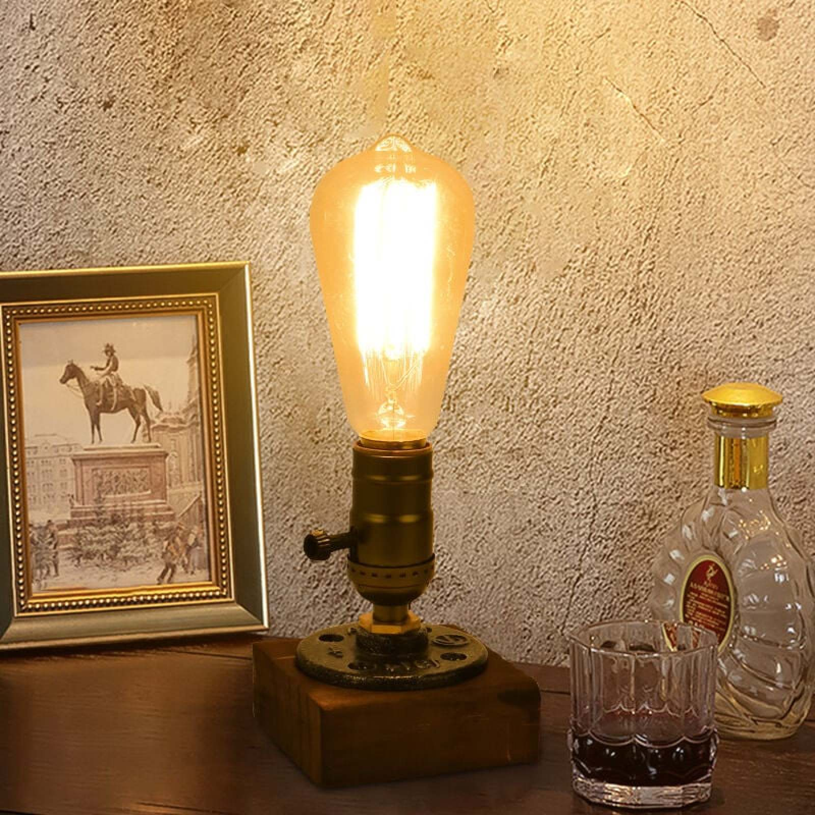 Eine Lampe mit Glühbirne, ein gerahmtes Bild und eine Flasche auf einem Tisch.