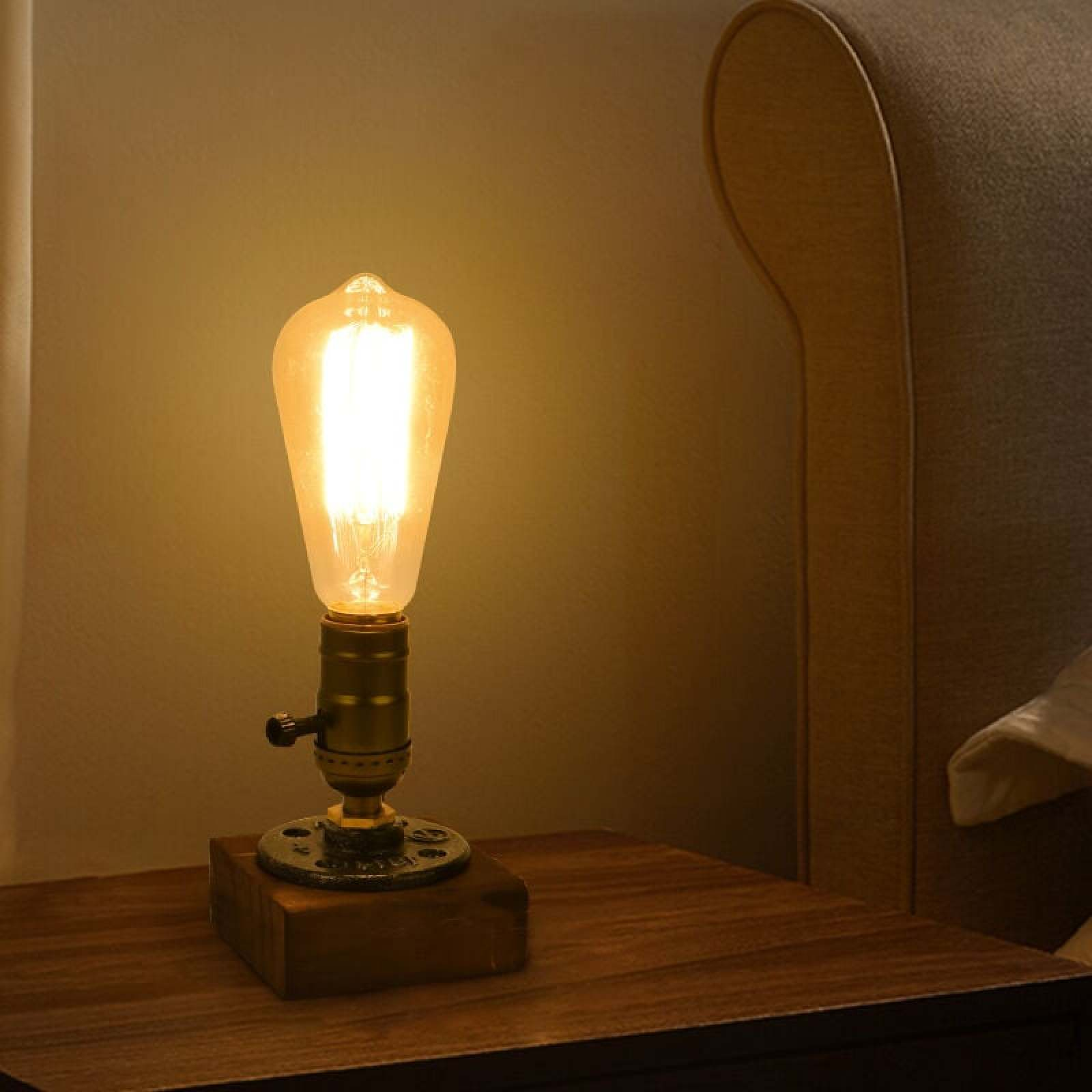 Eine Vintage-Glühbirnenlampe im Edison-Stil auf einem Nachttisch neben einem Bett.
