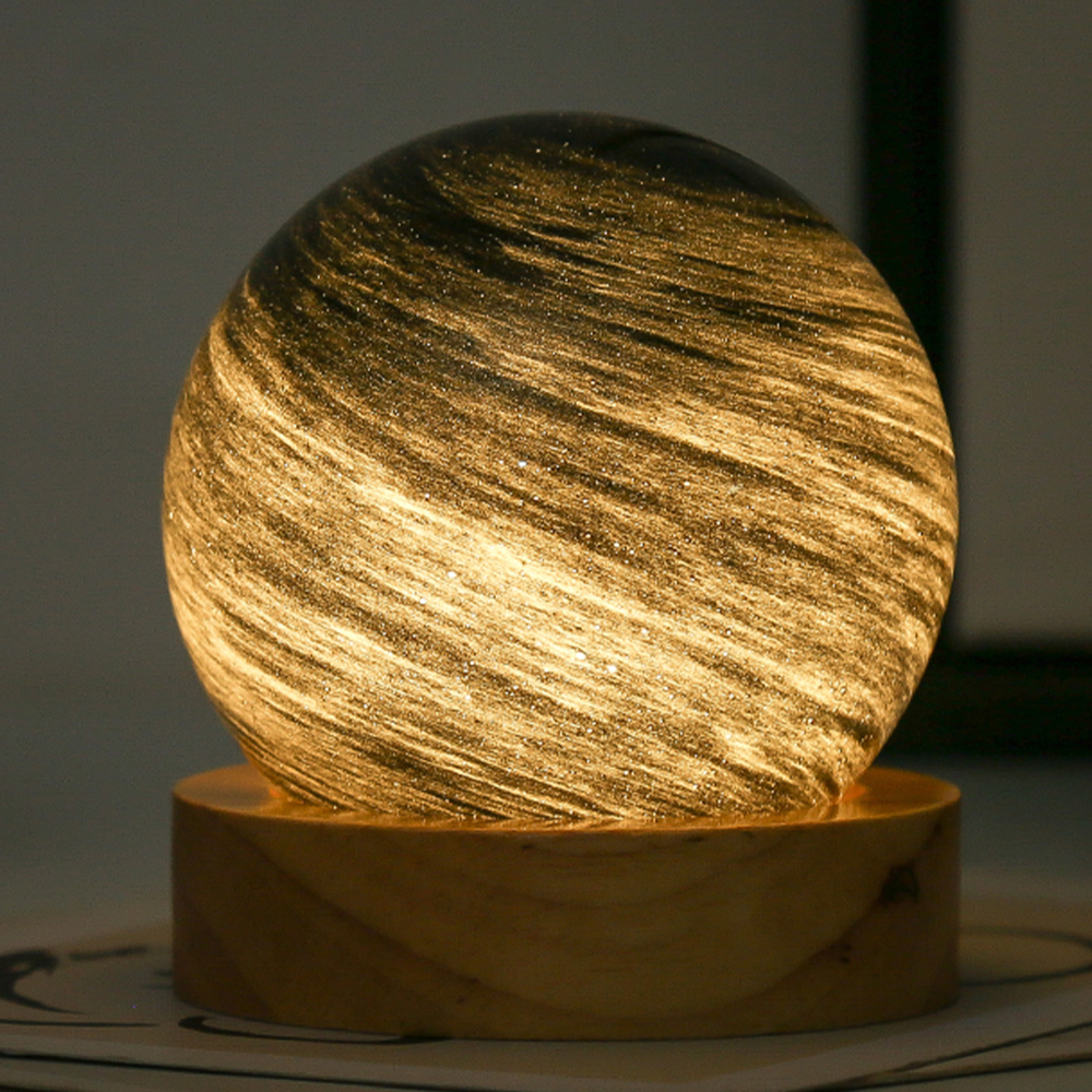 Eine beleuchtete Glaskugel mit Holzsockel und wirbelnden Mustern.