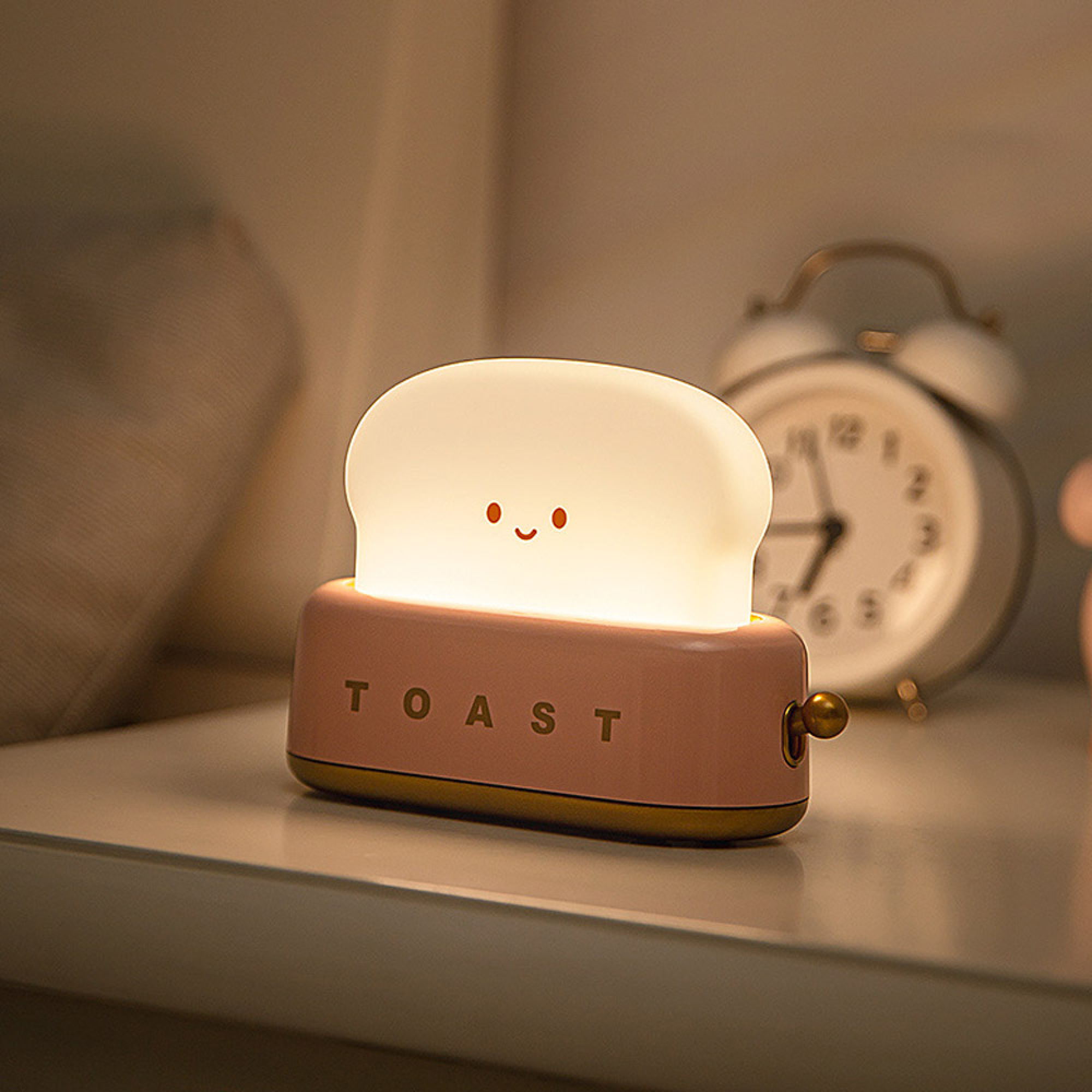 Eine rosa Toastlampe mit süßem Gesicht steht auf einem Regal neben einem Wecker.