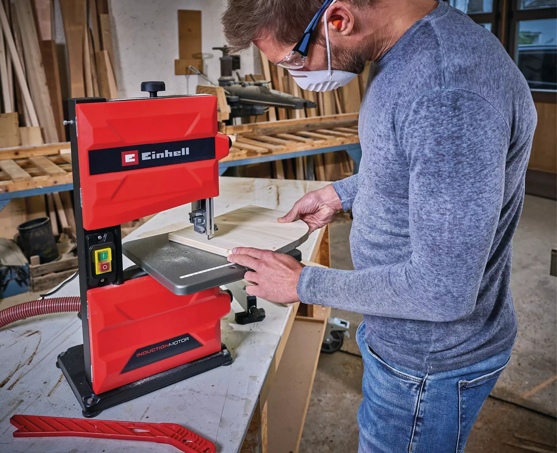 Mann sägt Holz auf roter Einhell-Bandsäge. Werkstatt im Hintergrund.