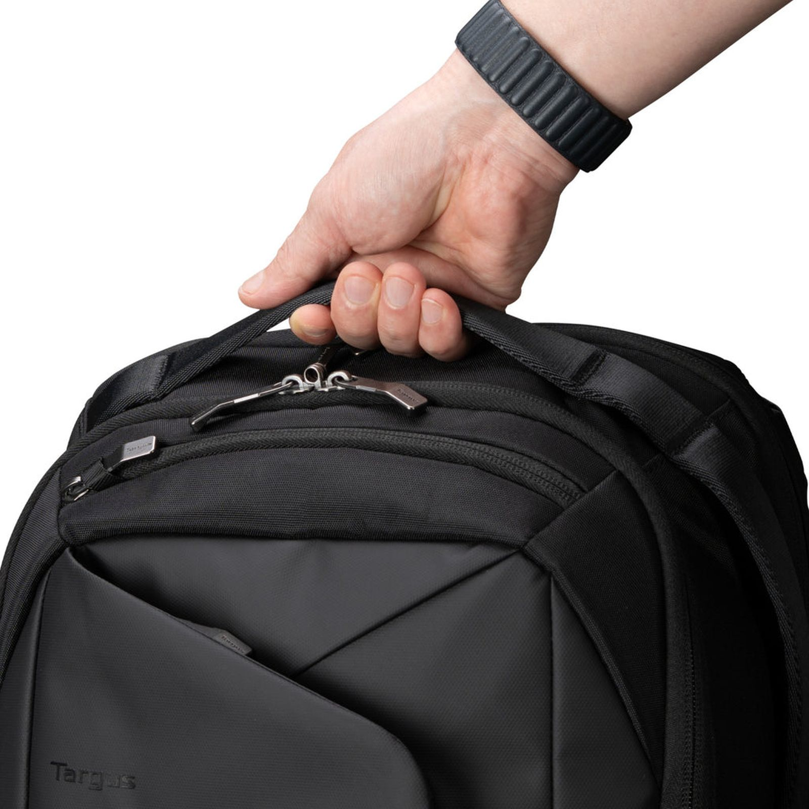 Eine Hand greift nach der oberen Schlaufe eines schwarzen Rucksacks mit Reißverschlüssen.