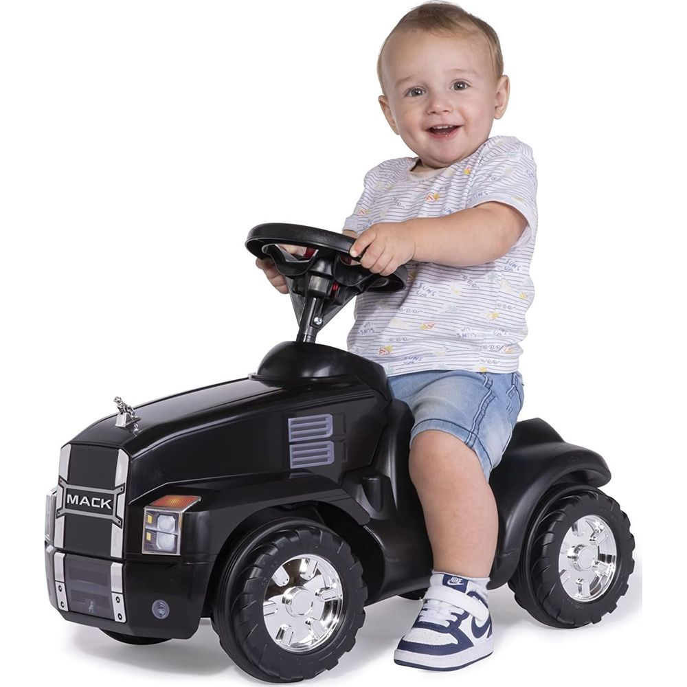 Ein lachendes Baby sitzt auf einem schwarzen Spielzeug-LKW mit Lenkrad und fährt.