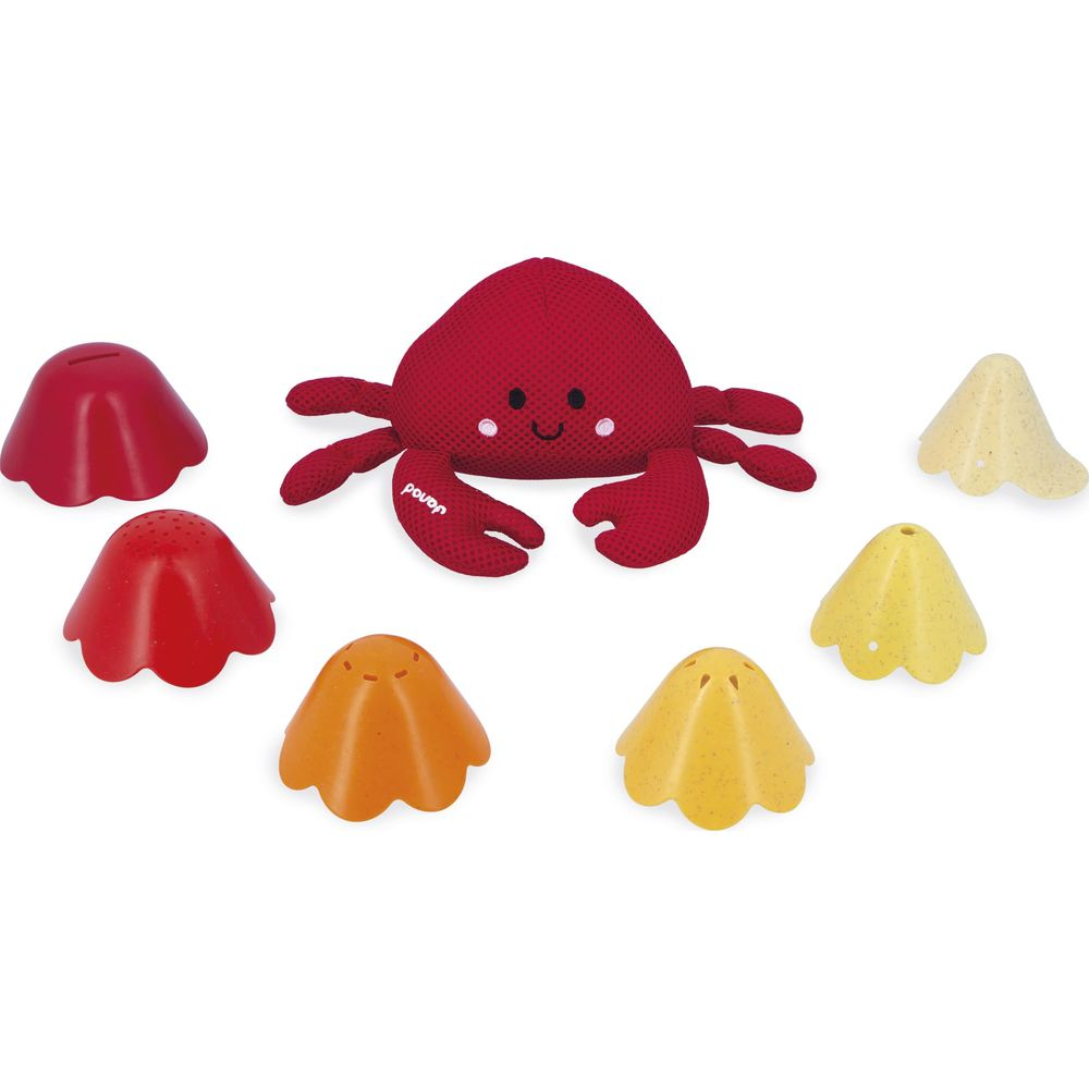 Ein roter Krabben-Plüschtier liegt umgeben von bunten Sandförmchen auf weißem Grund.