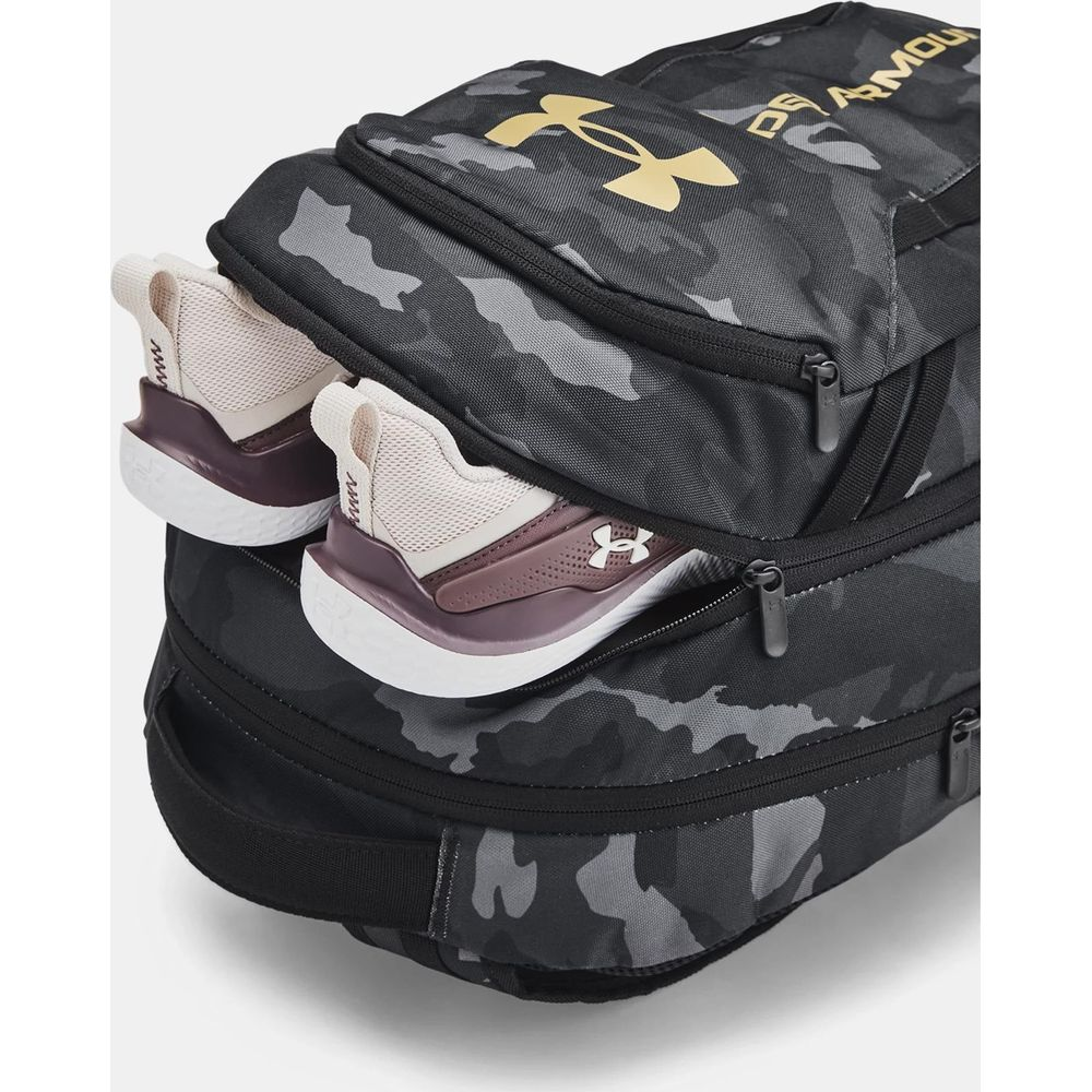 Zaino mimetico grigio con logo Under Armour dorato, scarpe che spuntano.