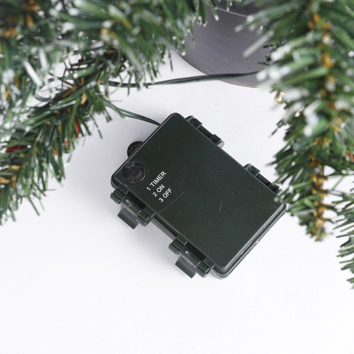 A green box with timer, on, and off options, under a Christmas tree.