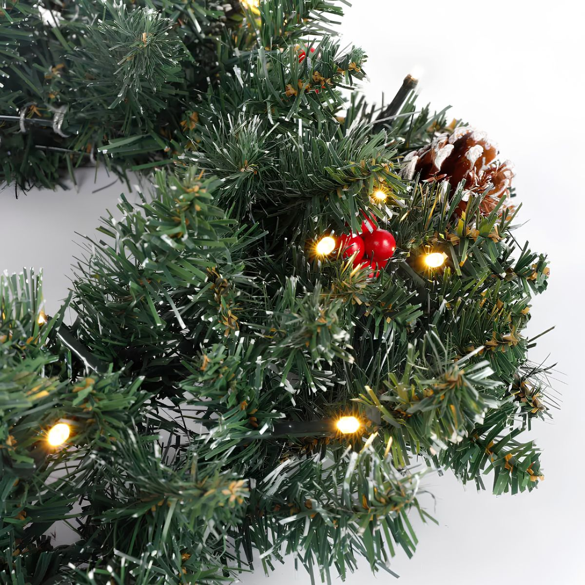 An artificial Christmas wreath with pinecones, red berries, and lights.