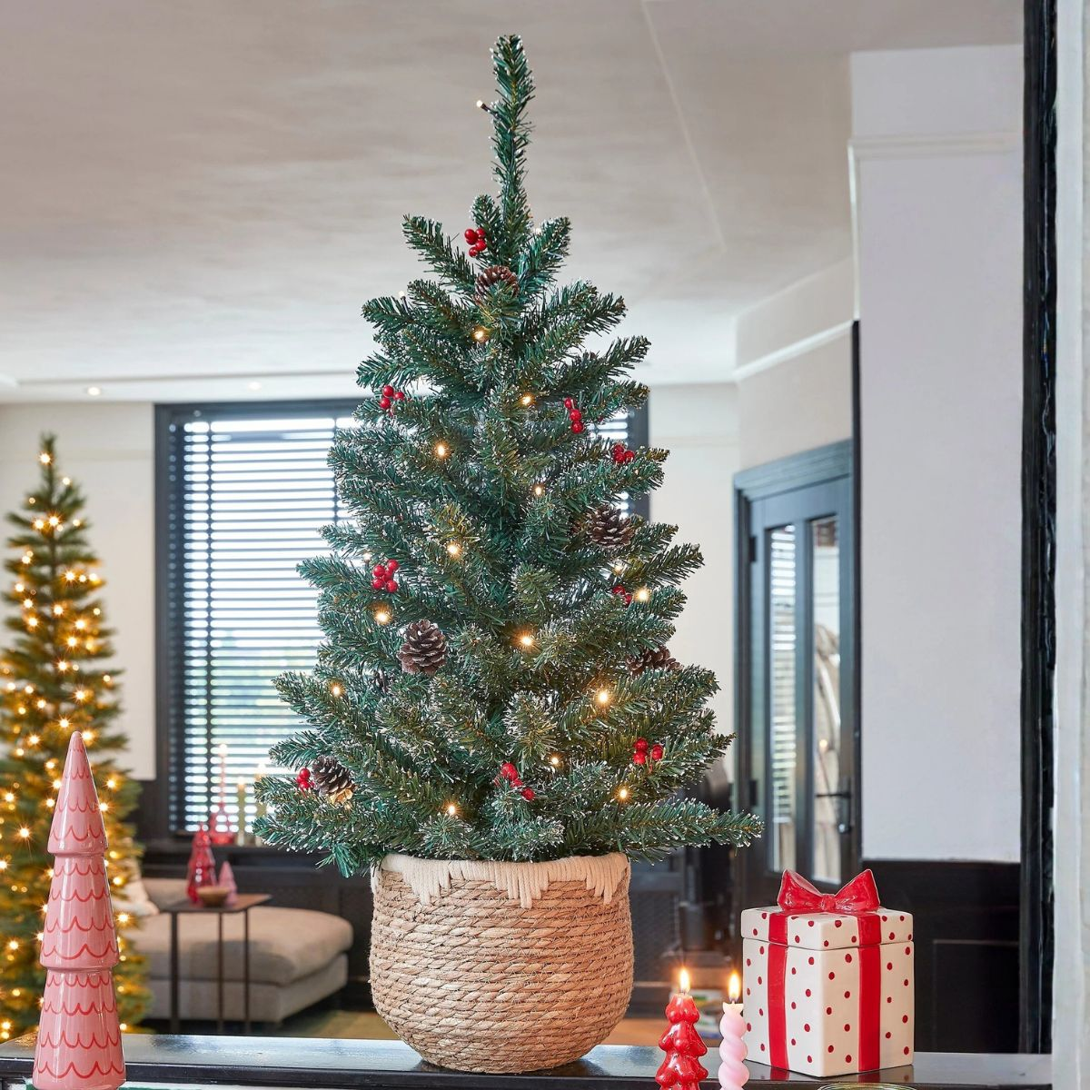 A decorated Christmas tree in a basket with lights, pinecones, and berries.