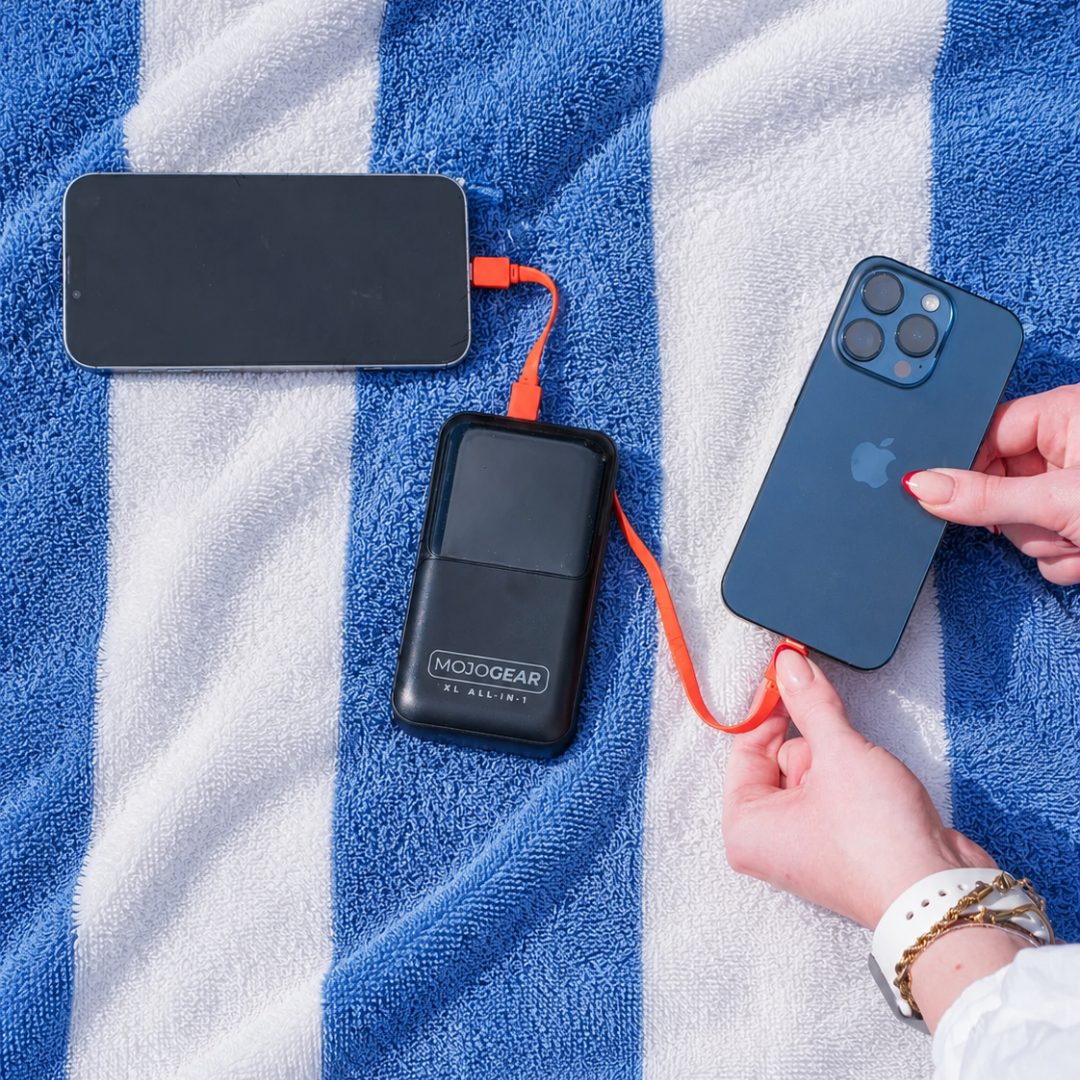 A black power bank charges two phones on a blue and white striped towel.