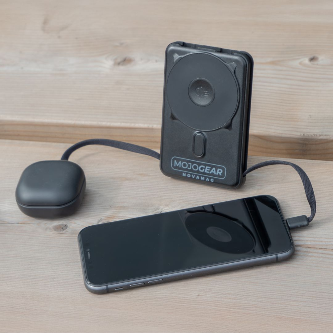 Schwarzes Smartphone wird mit einem schwarzen MagSafe-Ladegerät auf Holztisch geladen.