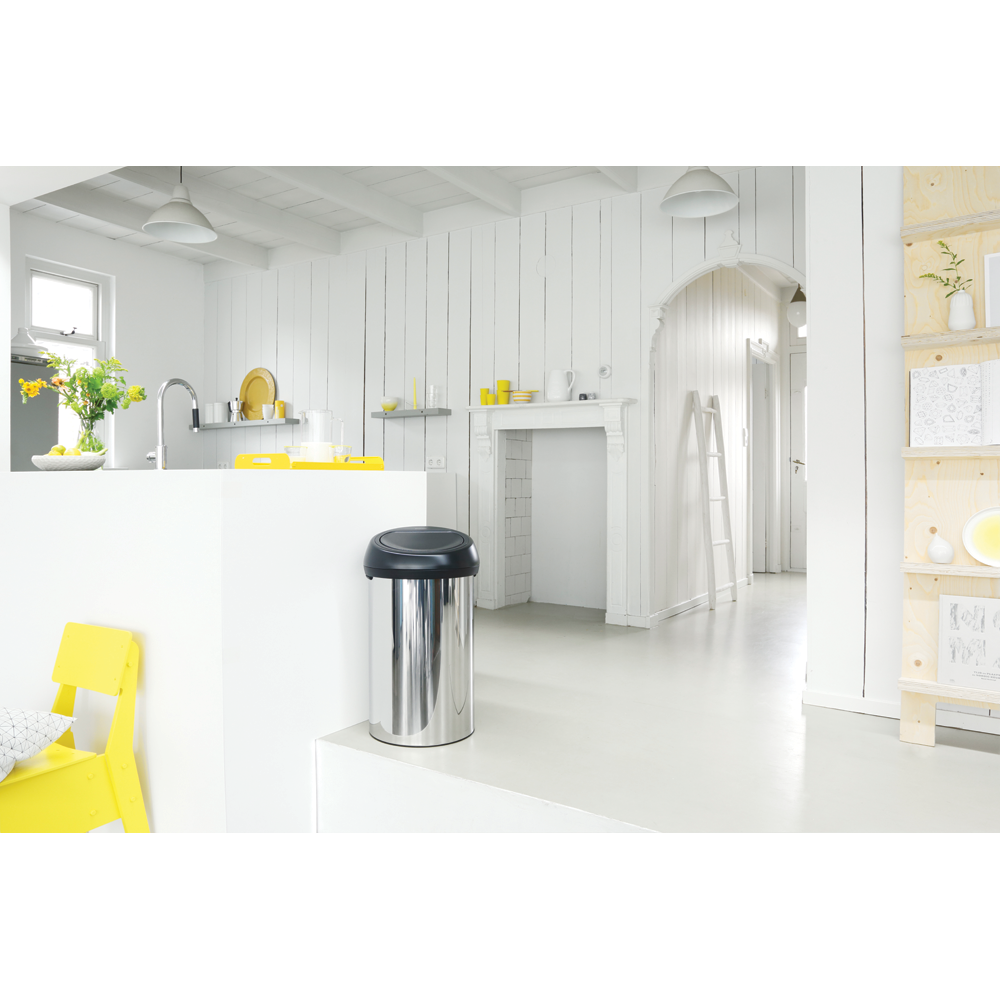 Une poubelle argentée brillante avec un couvercle noir dans une cuisine lumineuse avec des touches jaunes.