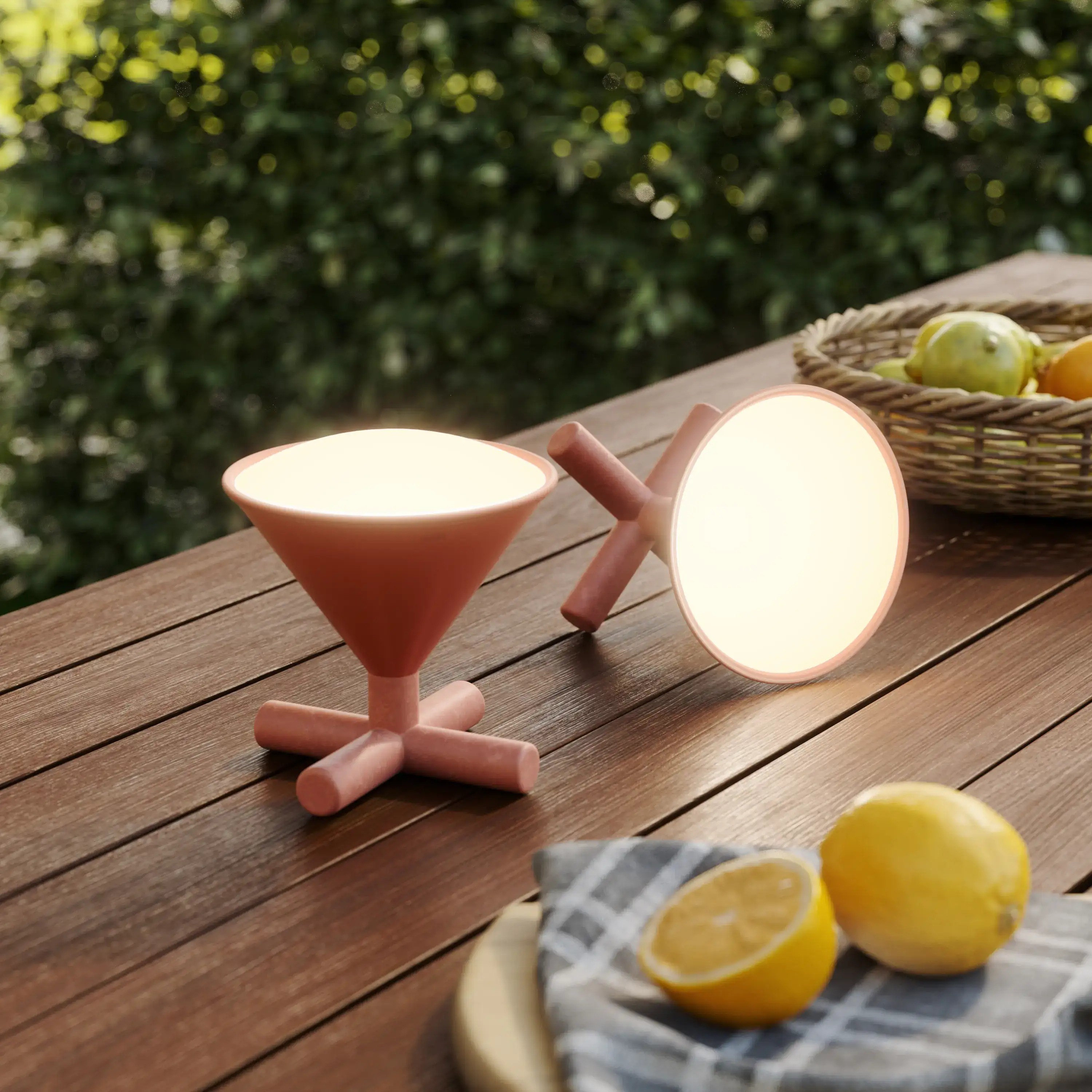 Due lampade rosa su tavolo di legno con frutta in un cesto sullo sfondo.