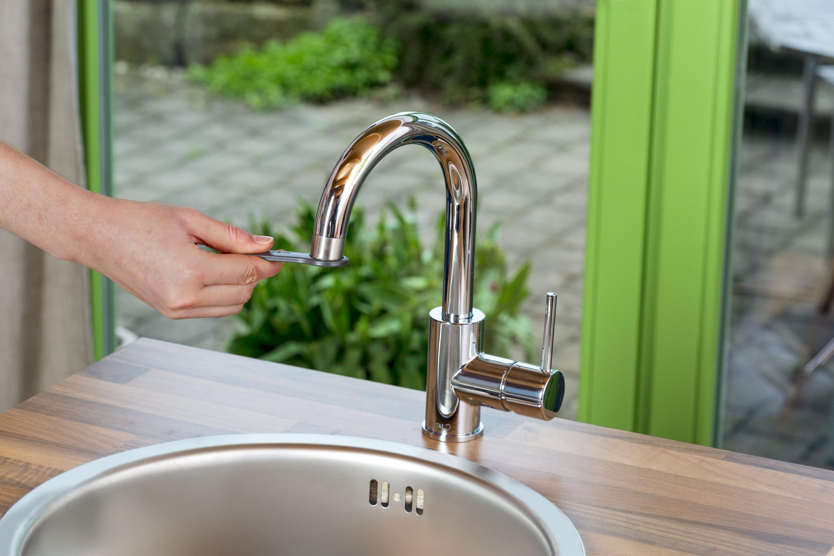 Eine Hand benutzt einen Schraubenschlüssel, um einen glänzenden Wasserhahn über einem Spülbecken zu reparieren.
