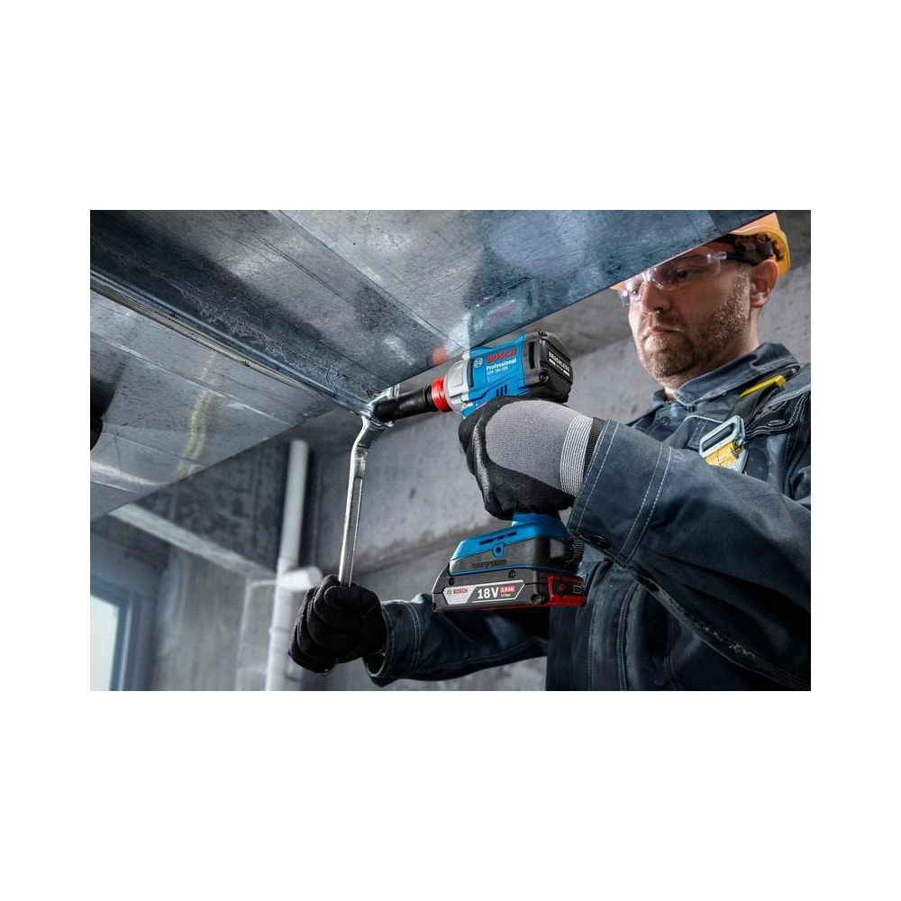Mann mit Schutzhelm benutzt Akkuschrauber an Metallträger.