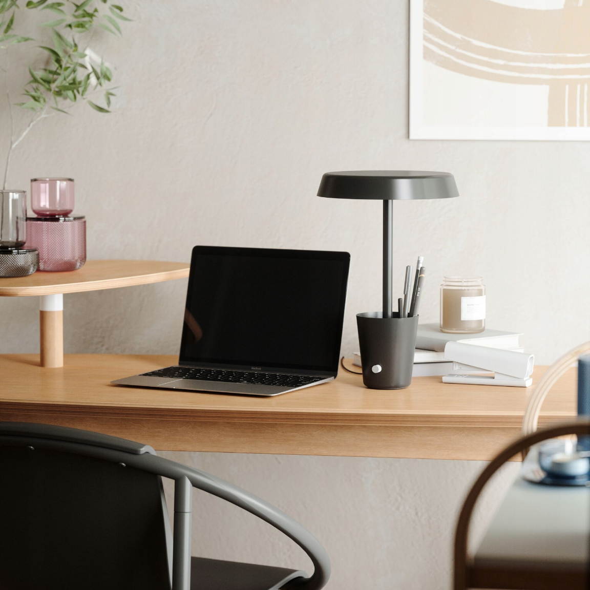 Un laptop aperto è su una scrivania accanto a un portapenne, una lampada e una candela.