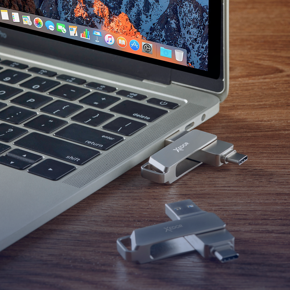 Two silver USB-C flash drives next to a laptop on a wooden table.
