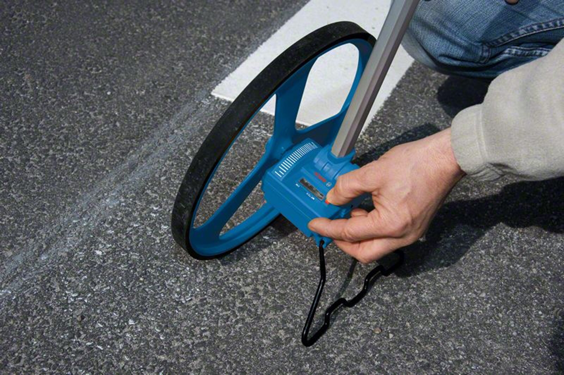 Eine Person benutzt ein blaues Messrad auf einer Asphaltstraße mit einer weißen Markierung.