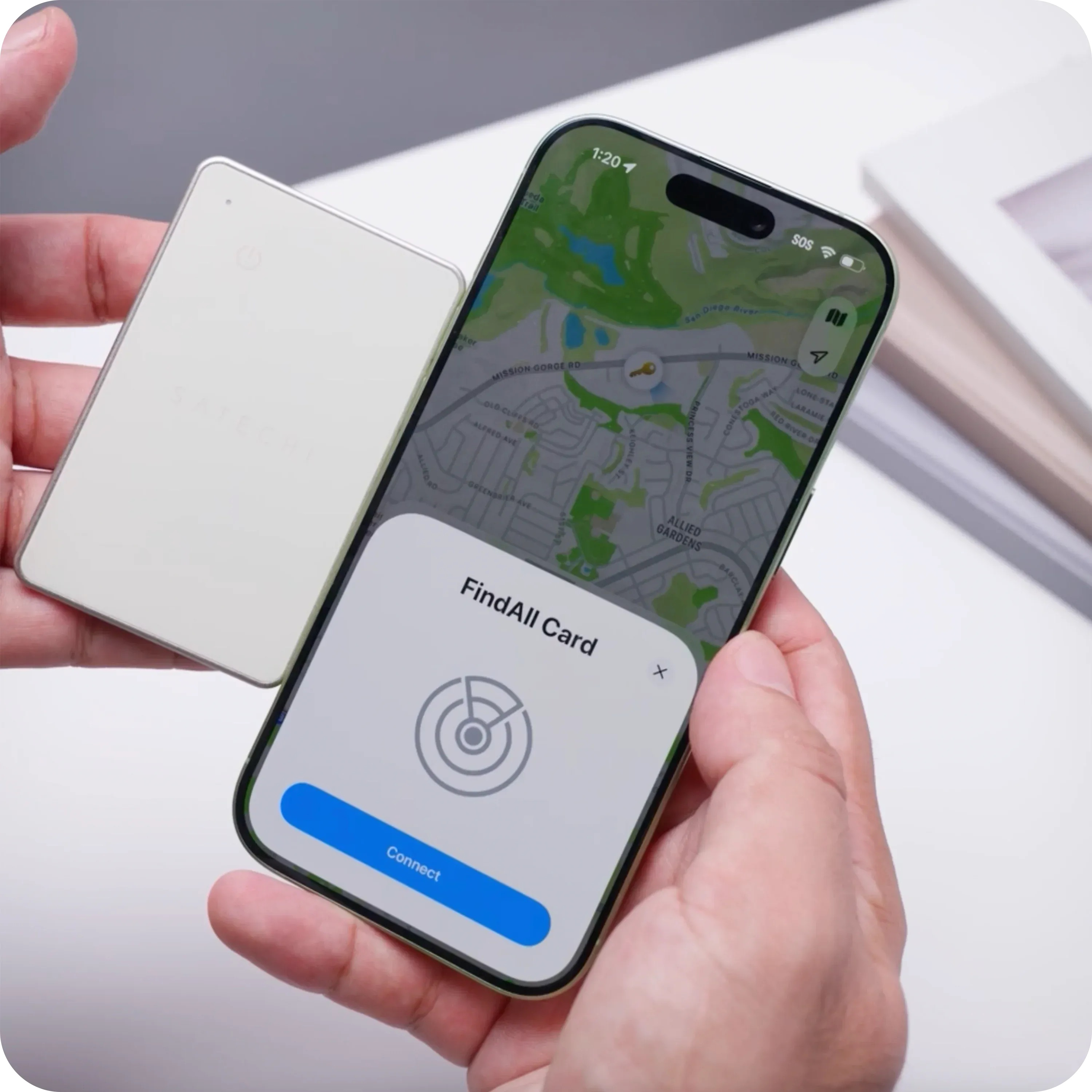 Dłoń trzyma białą kartę obok smartfona. Telefon wyświetla mapę i aplikację FindAll Card.