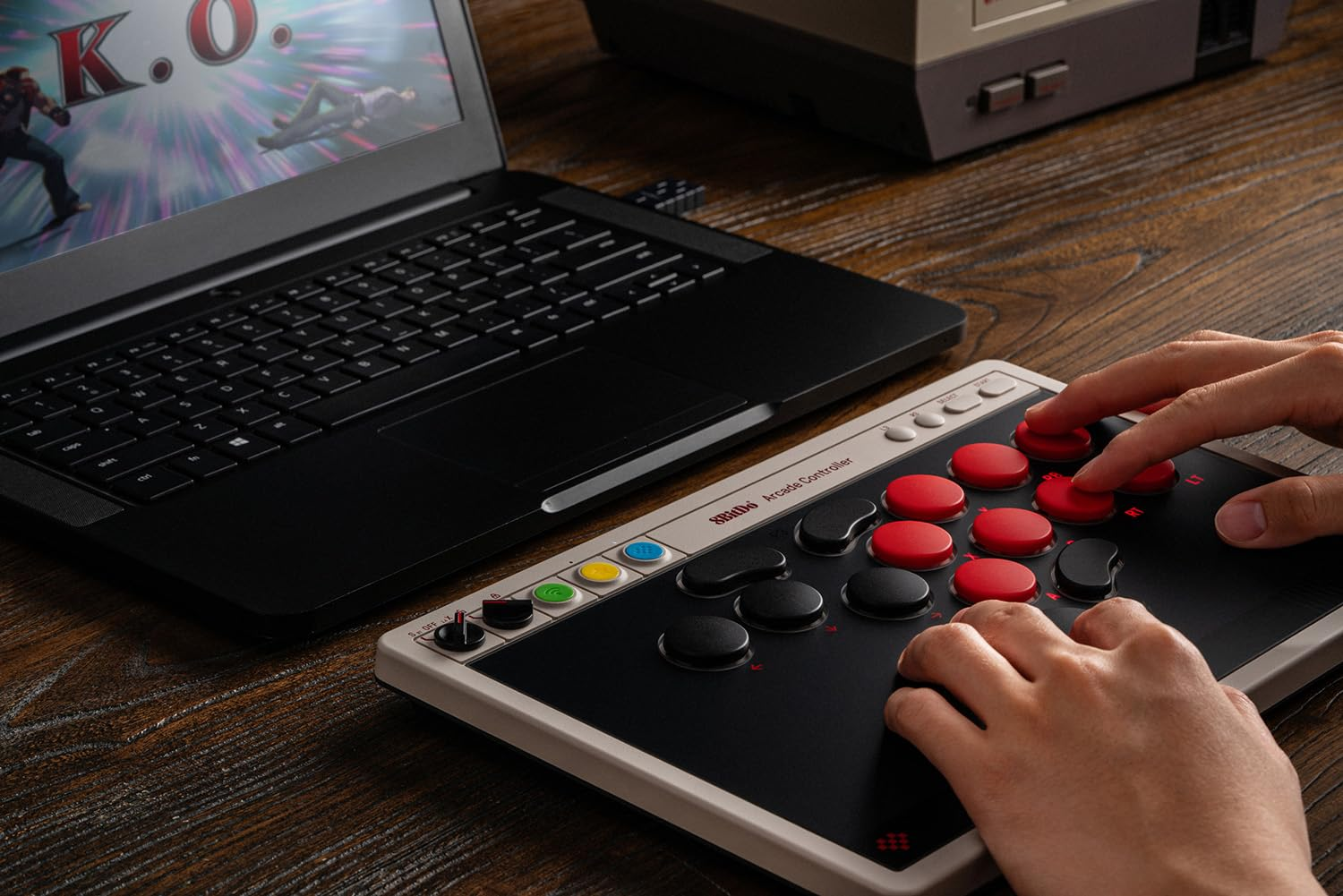 Dłonie obsługują kontroler zręcznościowy obok laptopa wyświetlającego grę walki.