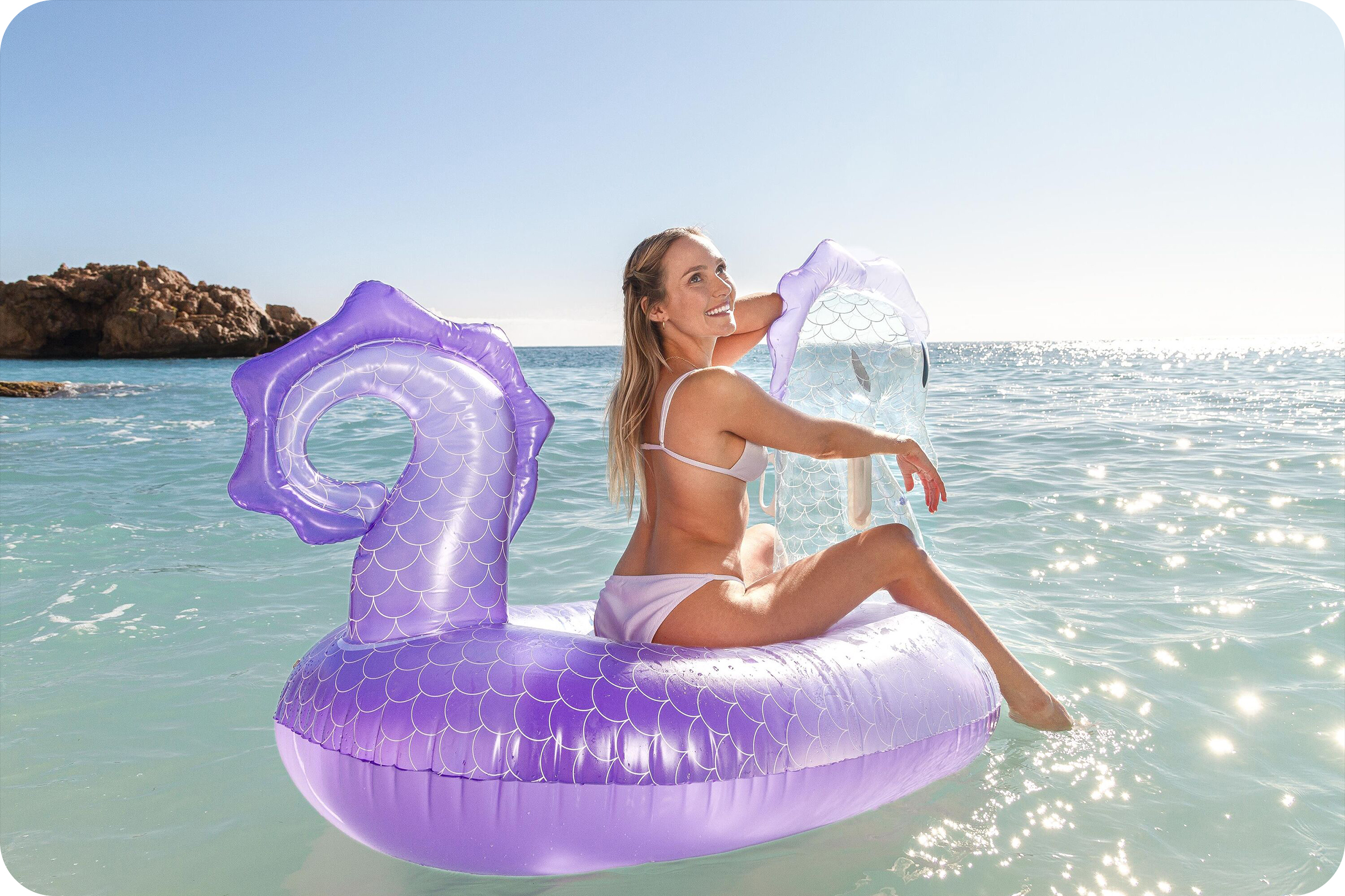 Kobieta w bikini na fioletowym dmuchanym smoku w oceanie.