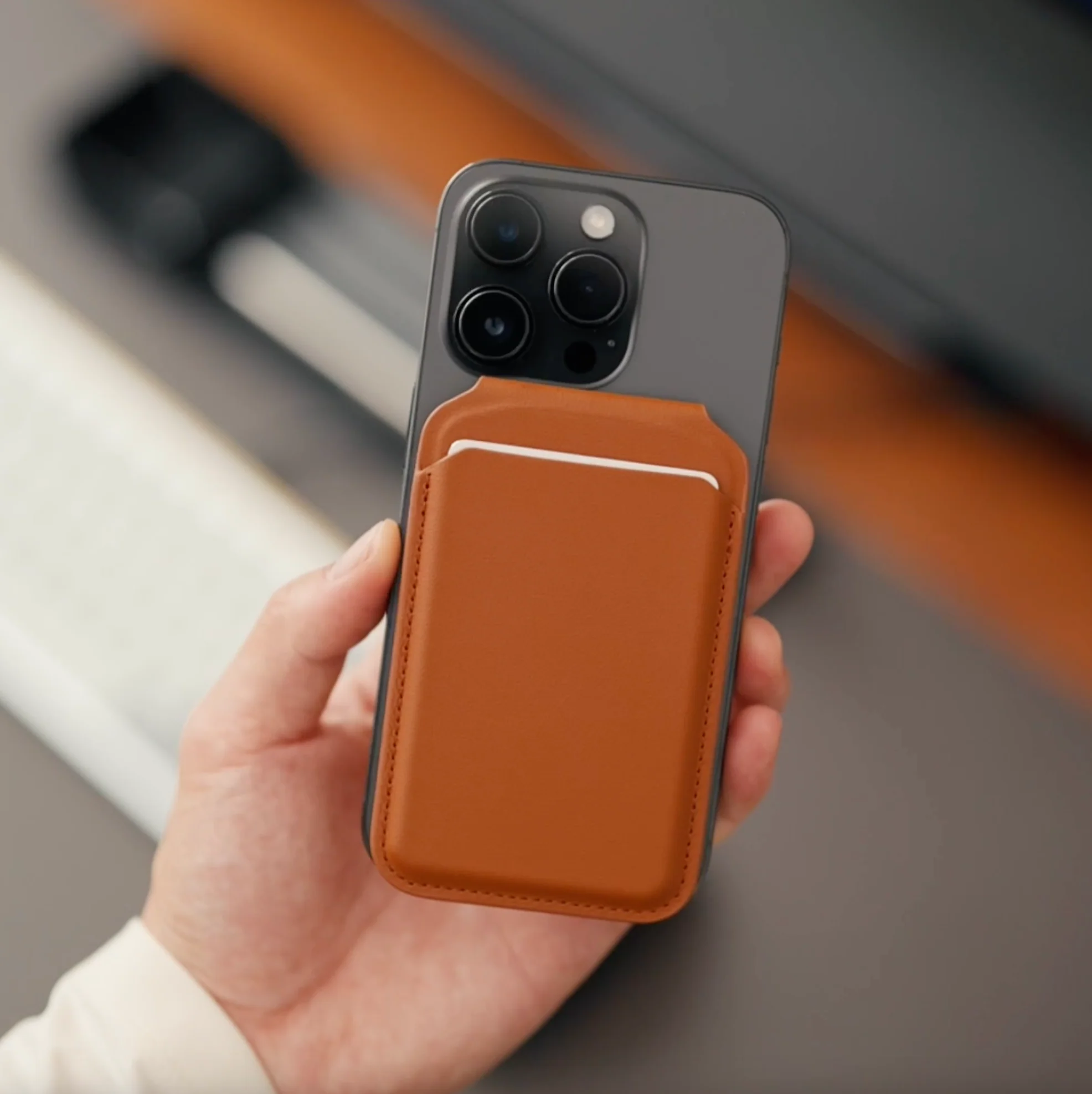 D łoń trzyma smartfon z brązowym skórzanym uchwytem na karty z tyłu.