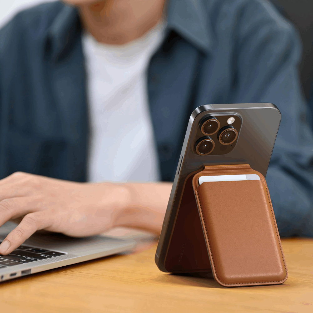 Telefon z brązowym skórzanym etui stoi na drewnianym biurku obok laptopa.
