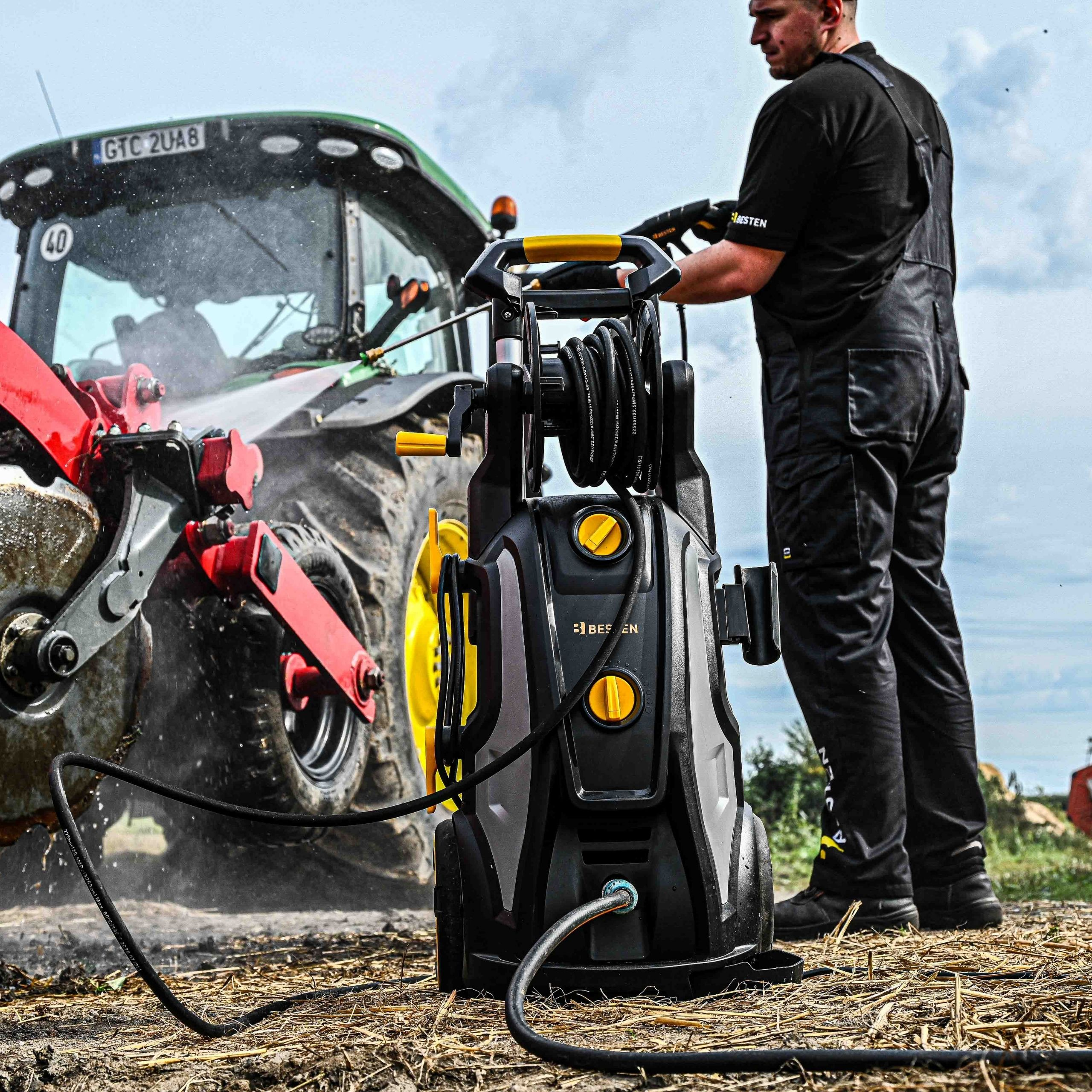 Mężczyzna czyści traktor myjką ciśnieniową na polu.