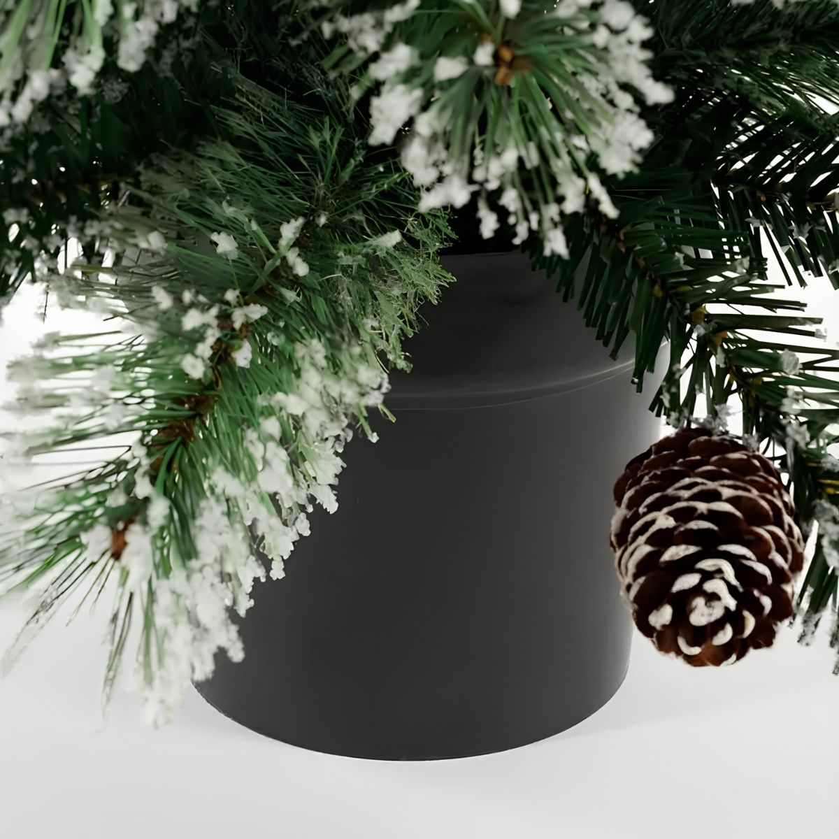 A pinecone hangs from a snow-dusted Christmas tree against a black pot.