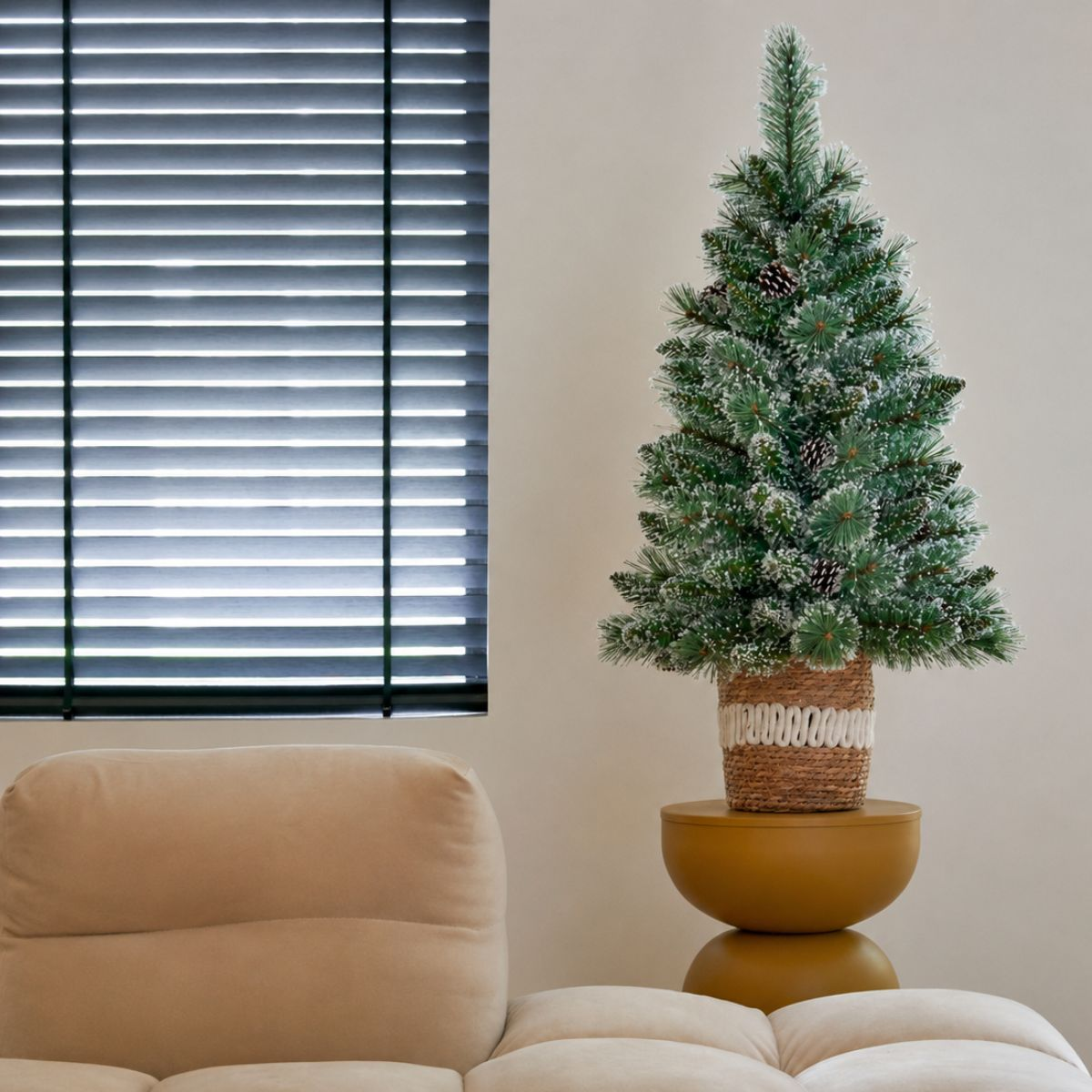 A small artificial Christmas tree with pinecones and snow, on a yellow stand.
