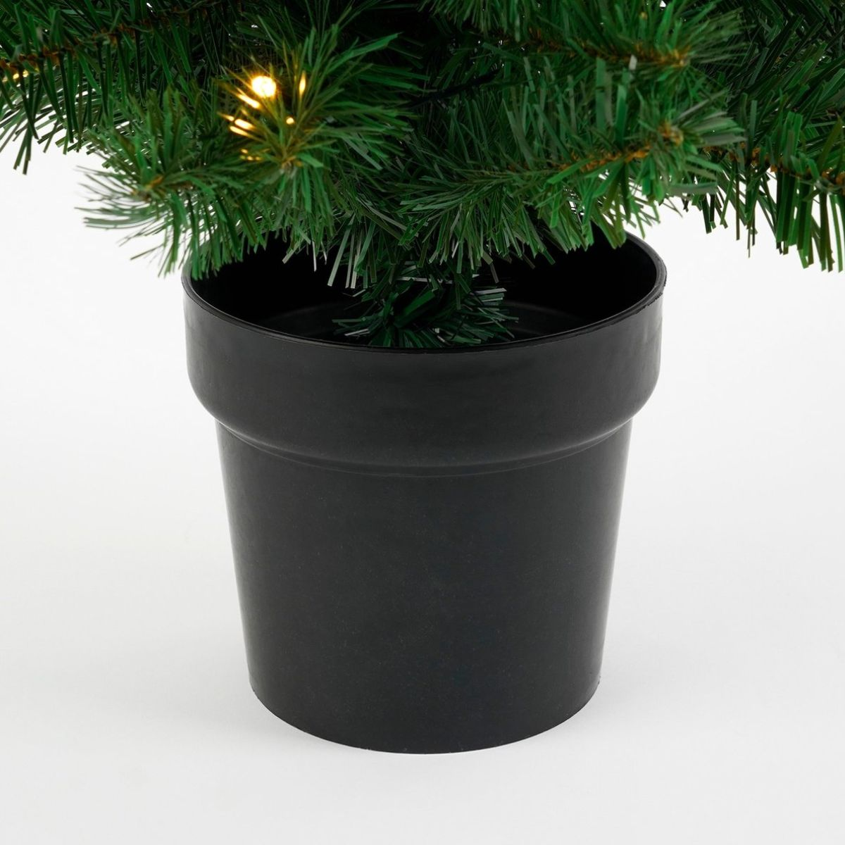Green artificial Christmas tree in a black pot with lights.