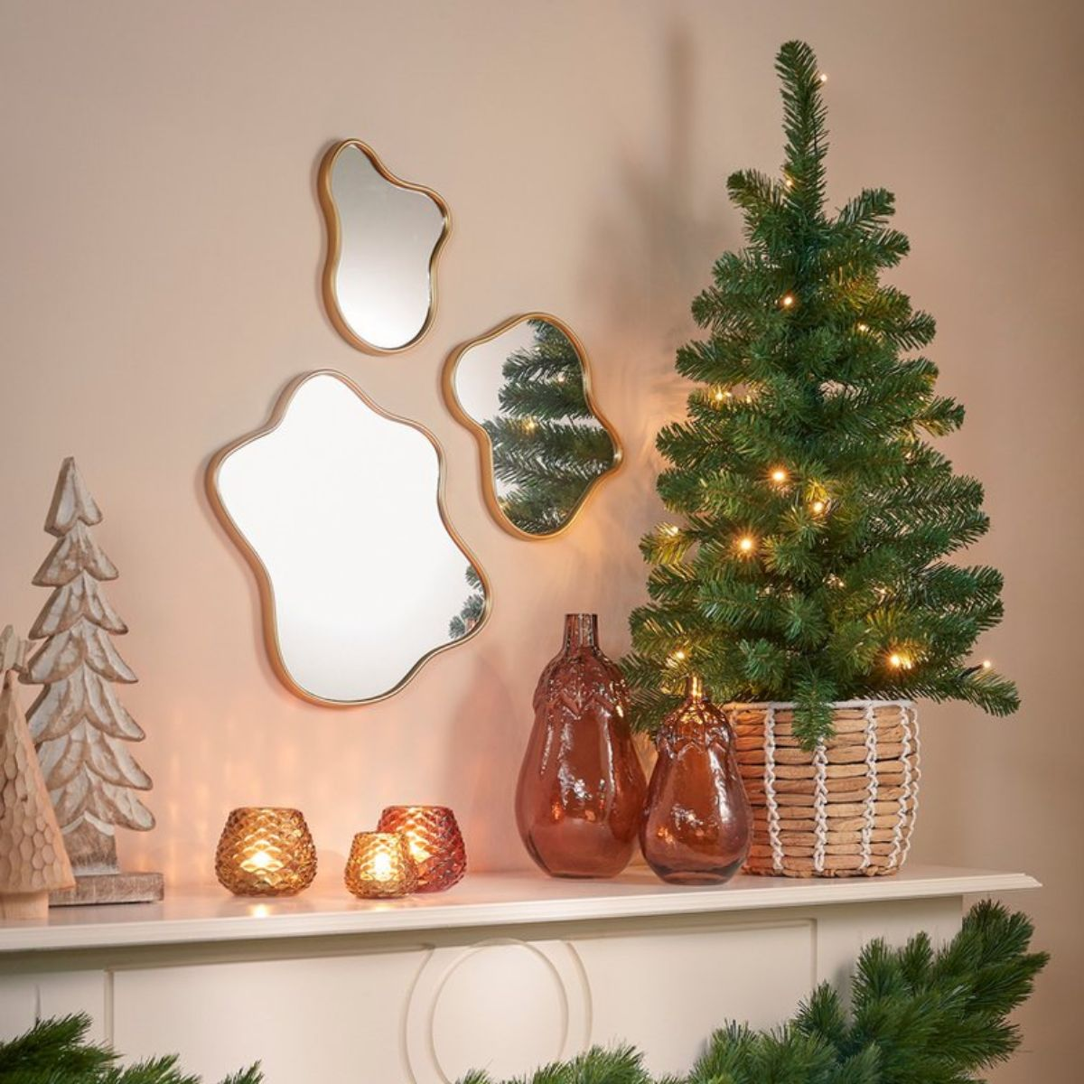 A Christmas tree with lights, mirrors, and decorations on a mantelpiece.