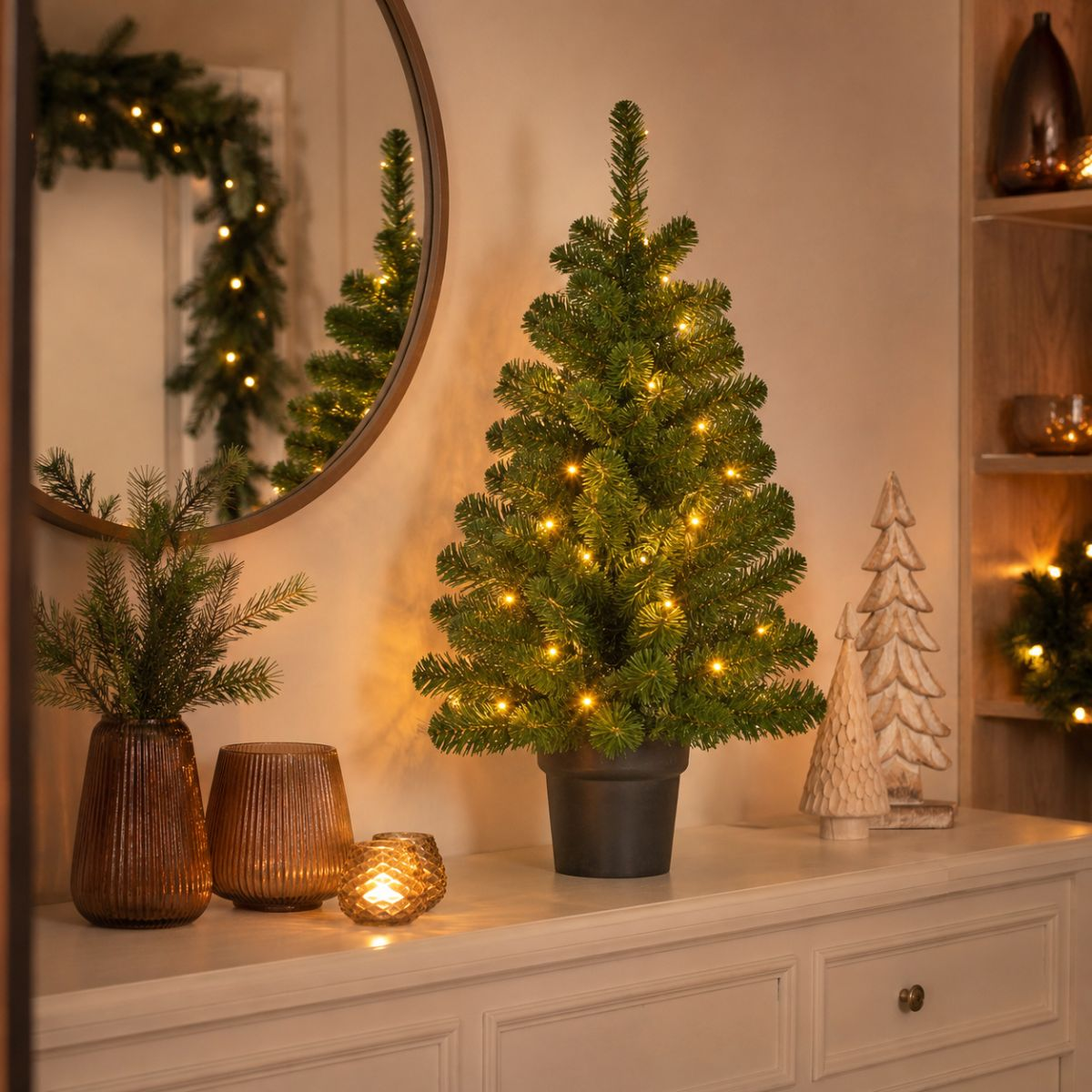 A small, lit Christmas tree sits on a dresser with decorative vases and candles.