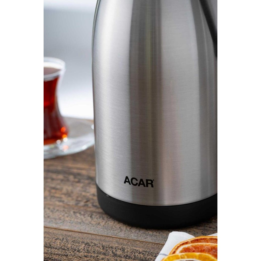 Siyah tabanlı gümüş termos, ahşap masa üzerinde bir bardak çayın yanında duruyor.