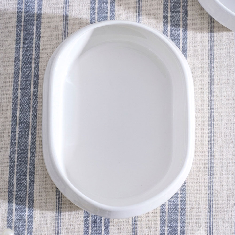 Çizgili kumaş üzerinde beyaz, oval seramik tabak.