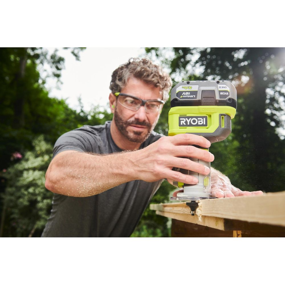 Mann mit Schutzbrille bearbeitet Holz mit einem Ryobi-Fräser im Freien.