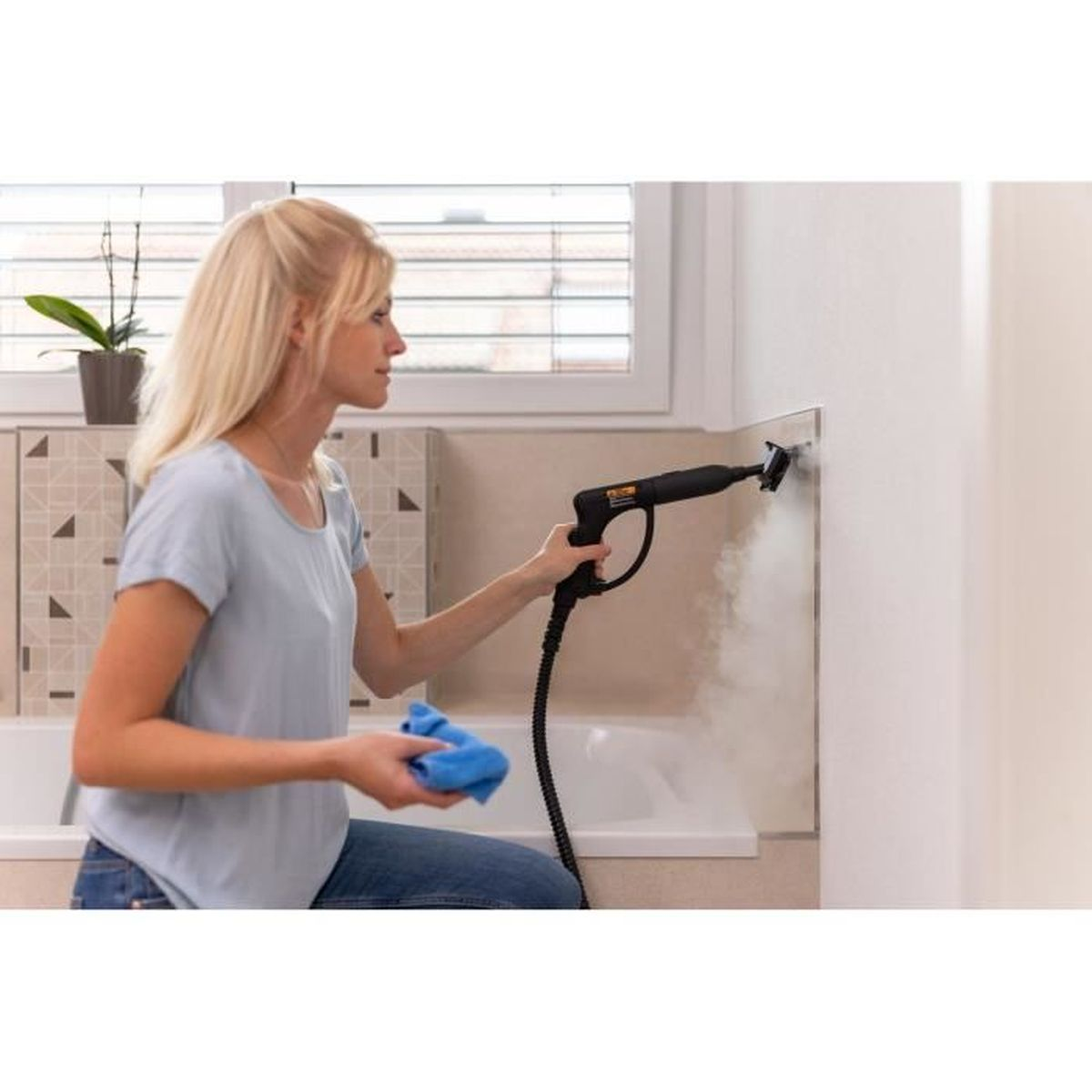 Eine Frau reinigt mit einem Dampfreiniger eine Wand neben einer Badewanne.
