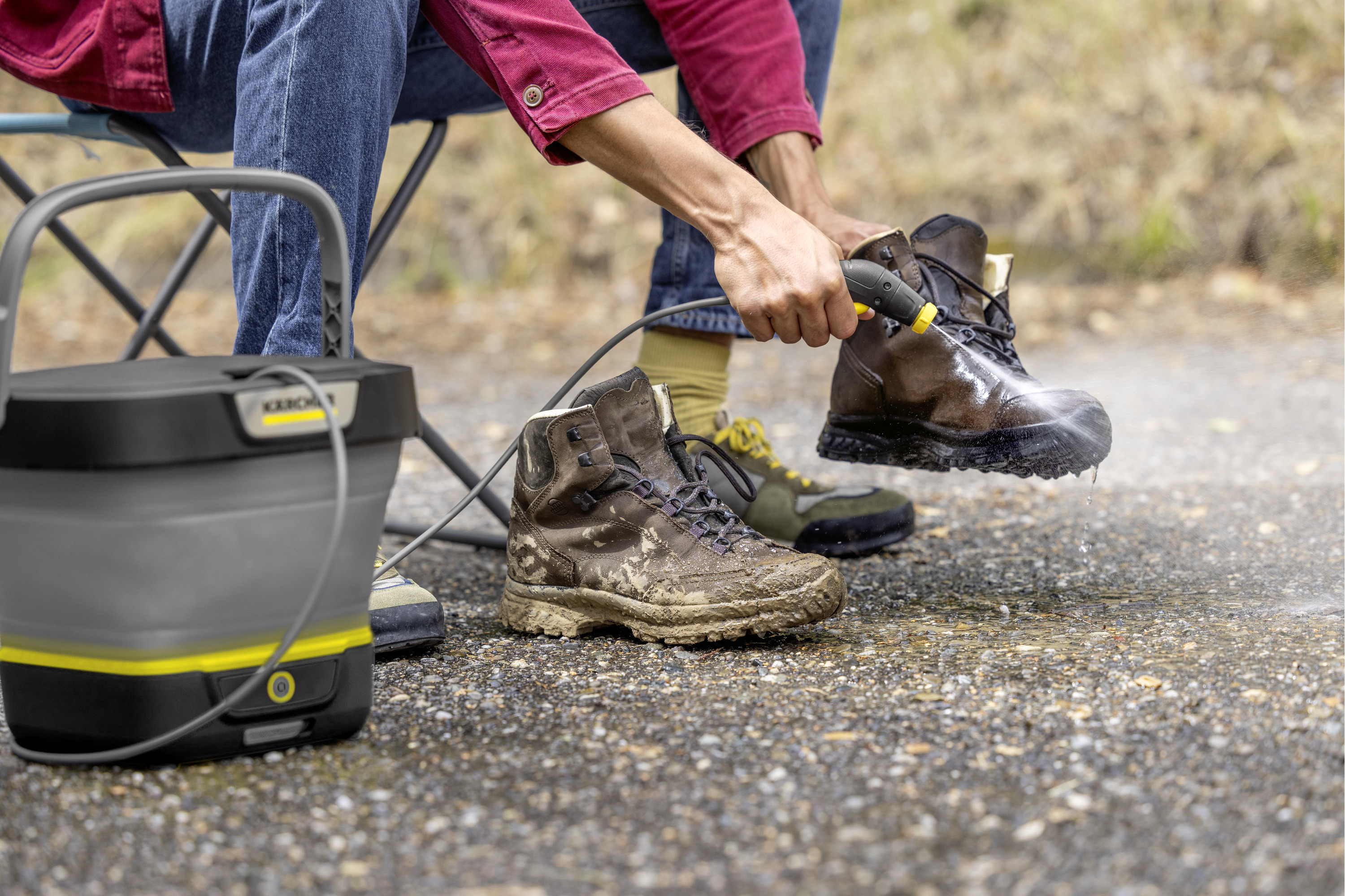 Person reinigt schlammige Wanderschuhe mit einem Hochdruckreiniger.