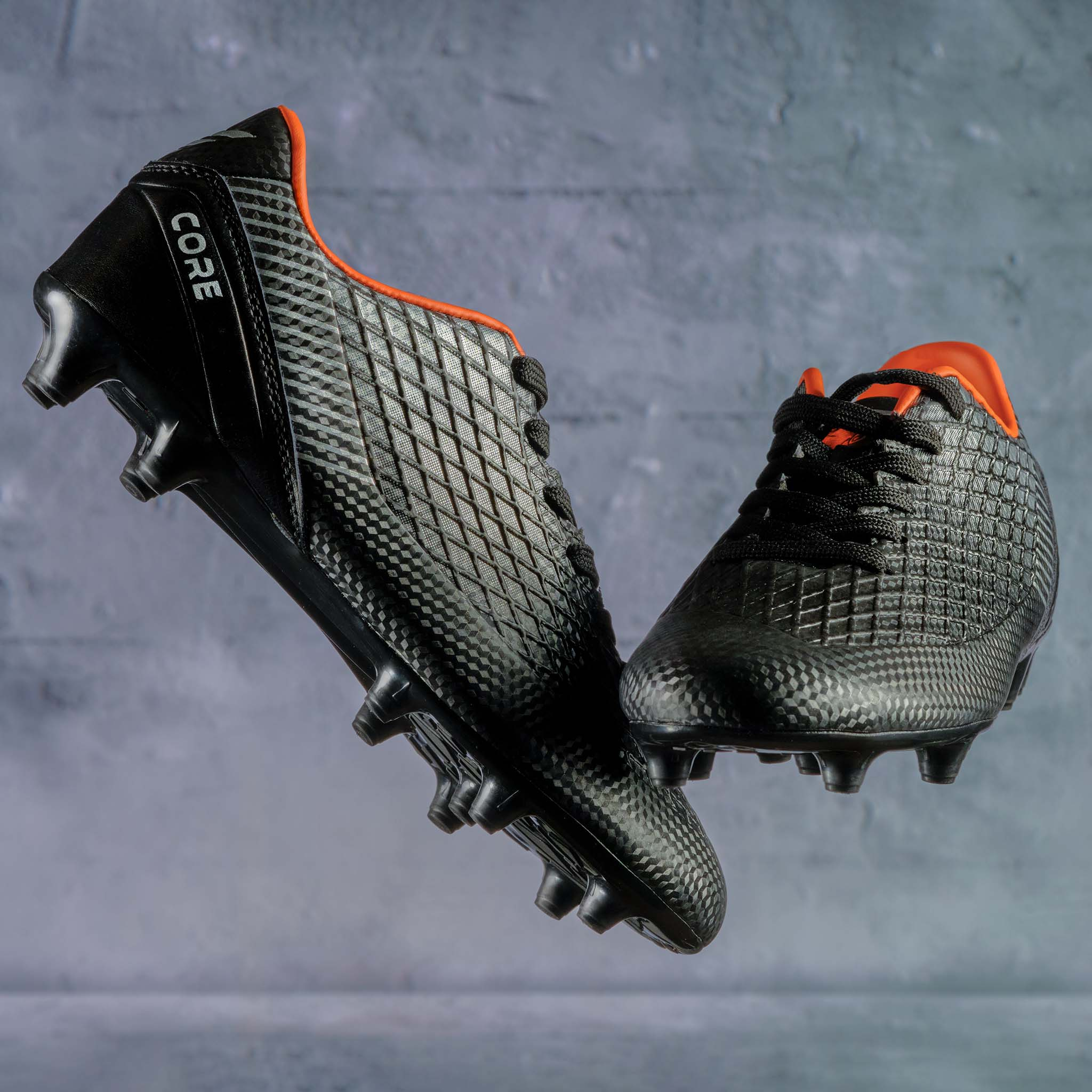 Schwarze Fußballschuhe mit orangefarbenen Akzenten schweben vor grauem Hintergrund.
