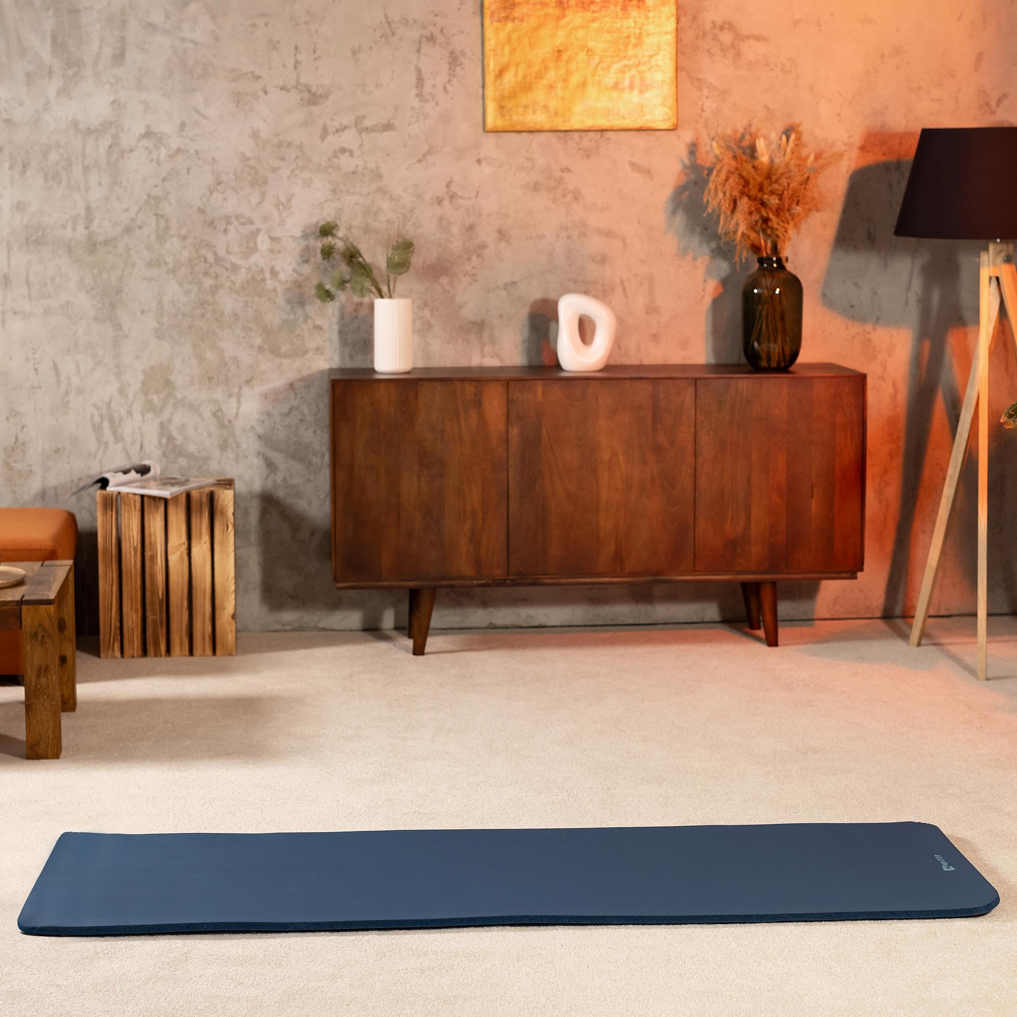 Eine dunkelblaue Yogamatte liegt auf einem hellen Teppich. Ein Holzkonsolentisch steht im Hintergrund.