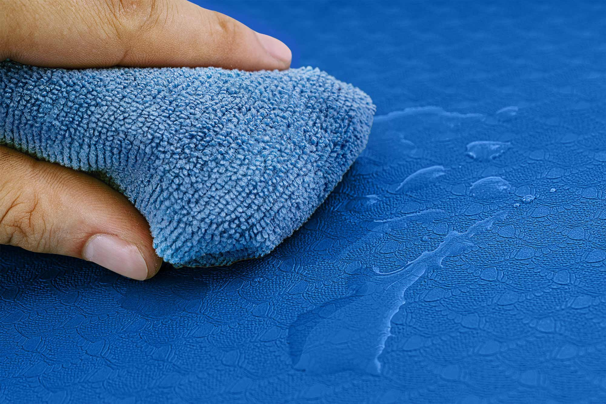 Eine Hand hält ein blaues Mikrofasertuch, das über eine blaue Oberfläche wischt.