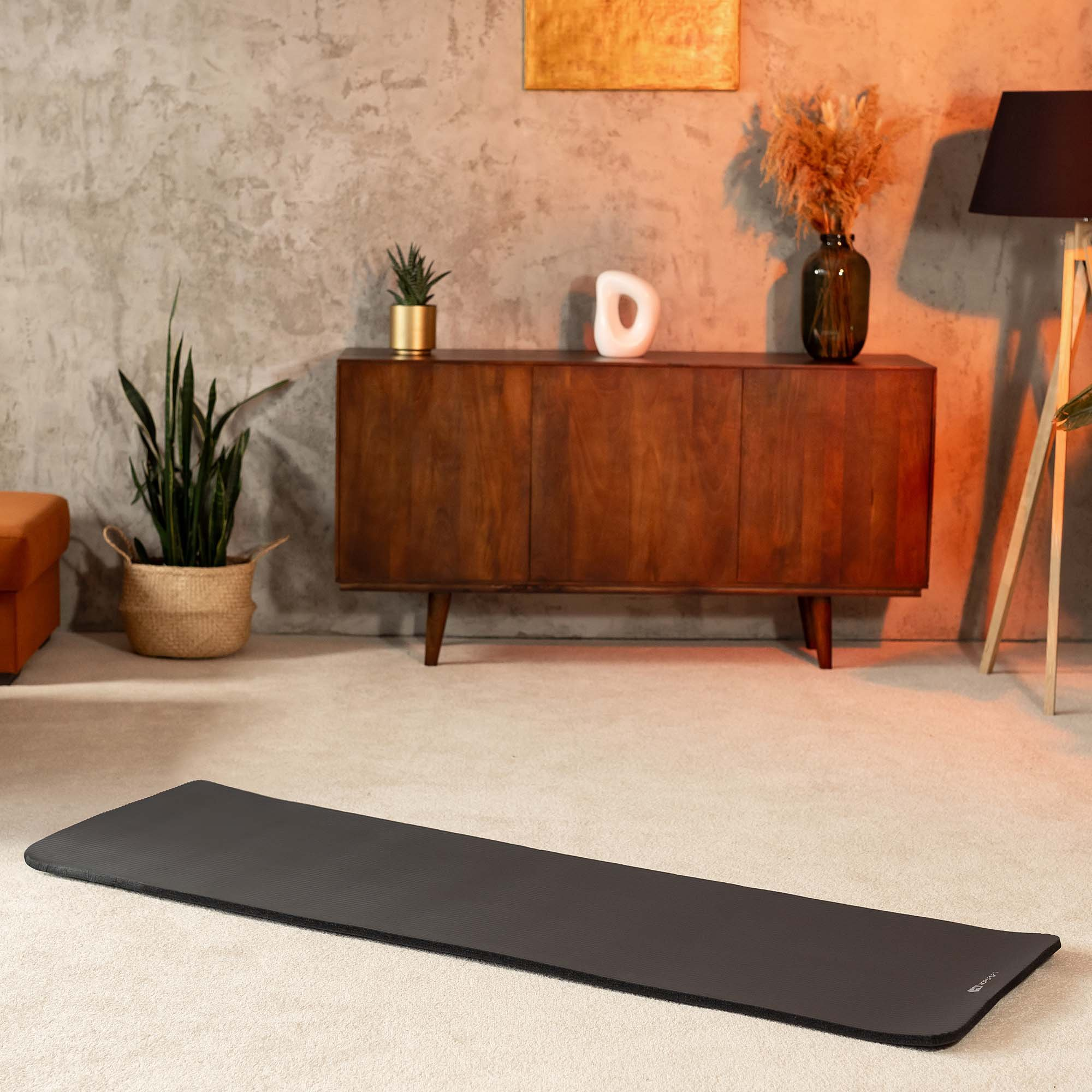 Eine dunkle Yogamatte liegt auf einem hellen Teppich vor einem Holzschrank.