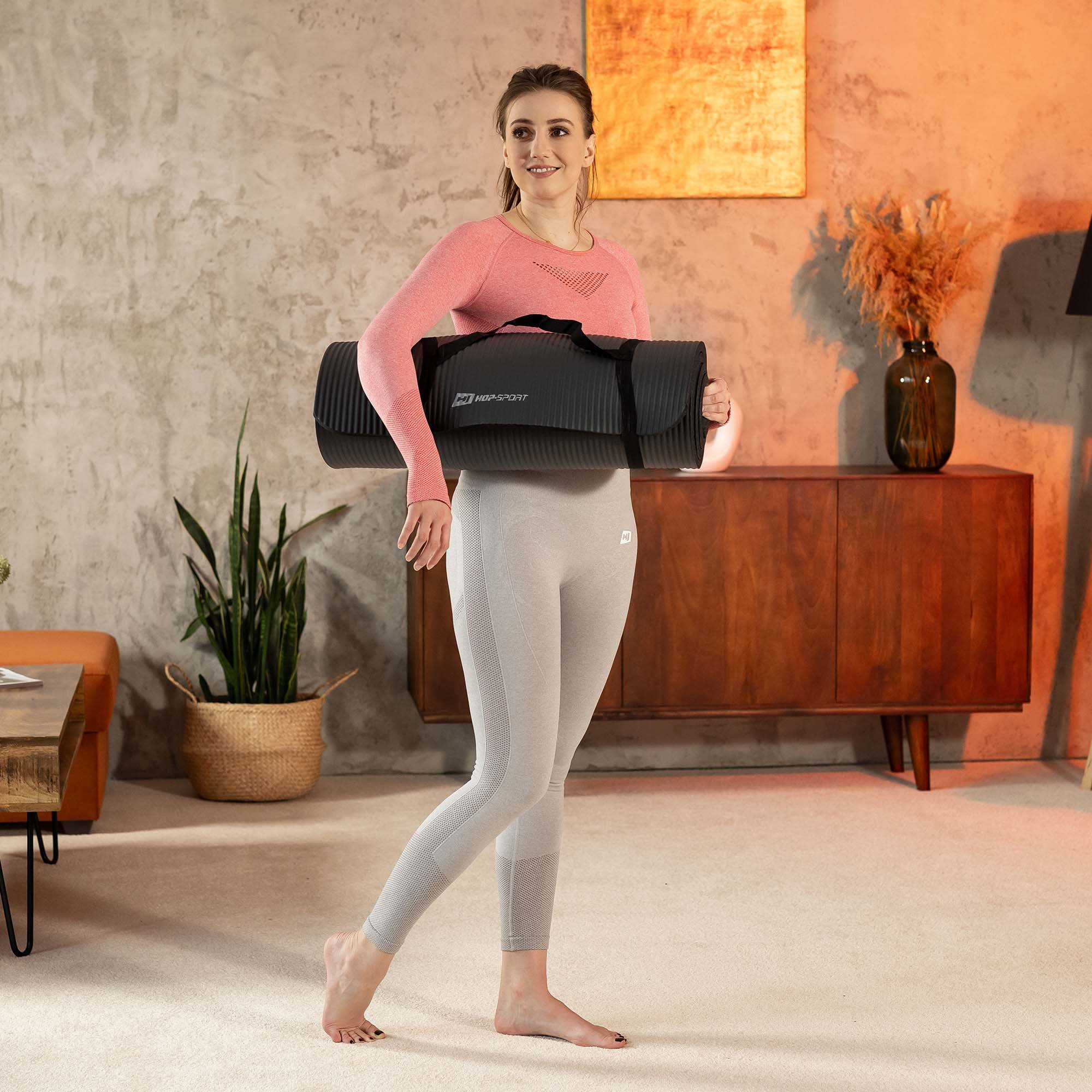 Frau trägt eine schwarze Yogamatte, gekleidet in pink und grau.