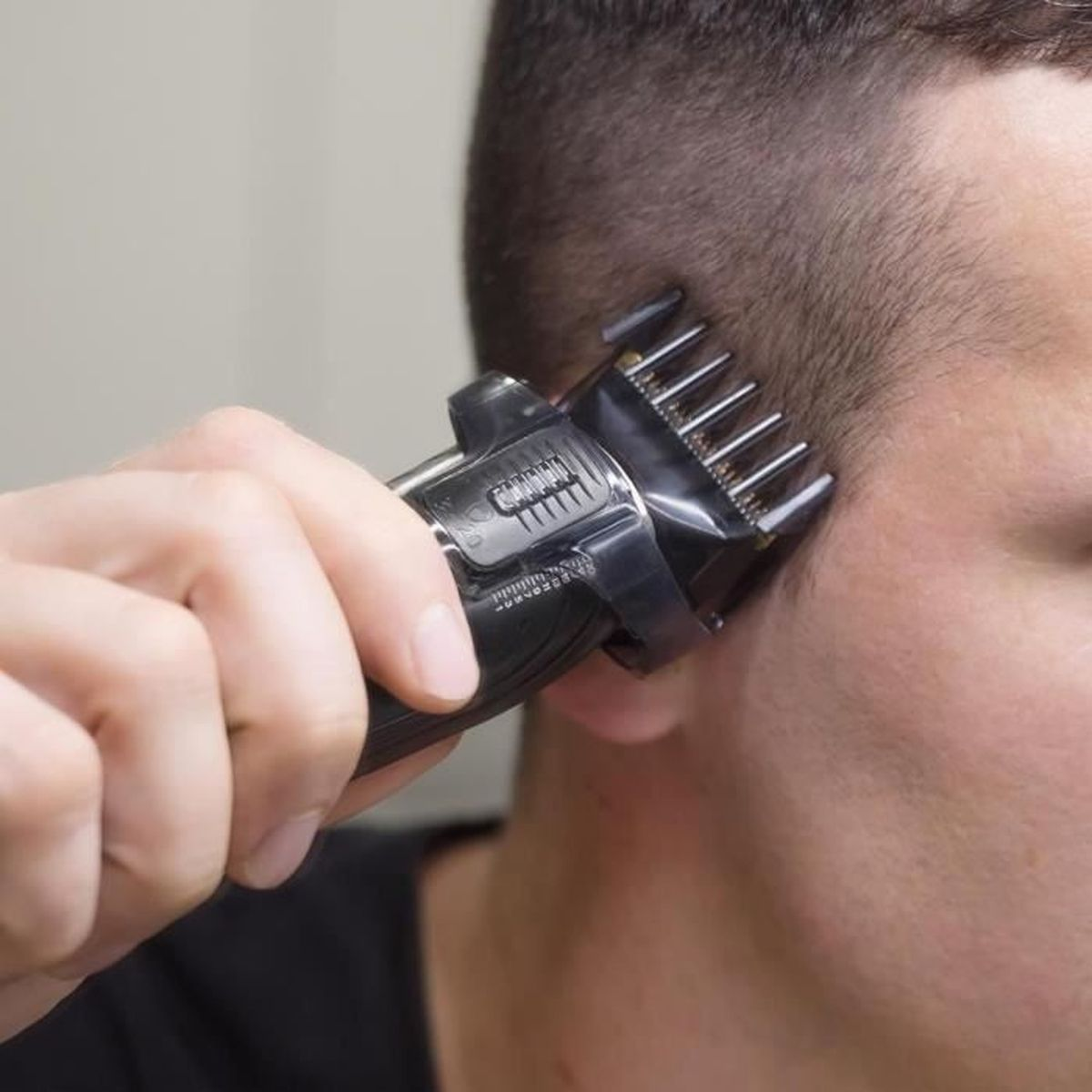 Eine Hand benutzt einen schwarzen Haarschneider, um das Haar am Kopf einer Person zu schneiden.