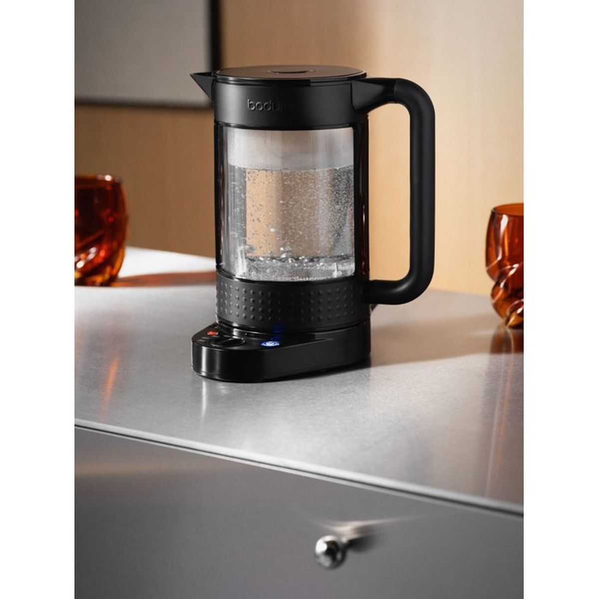 Hervidor eléctrico negro con jarra de cristal, lleno de agua, sobre encimera metálica.