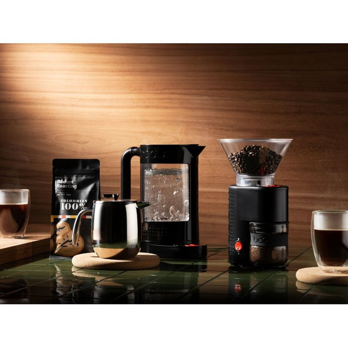 Cafetera, molinillo, café molido y dos tazas de café sobre una mesa.