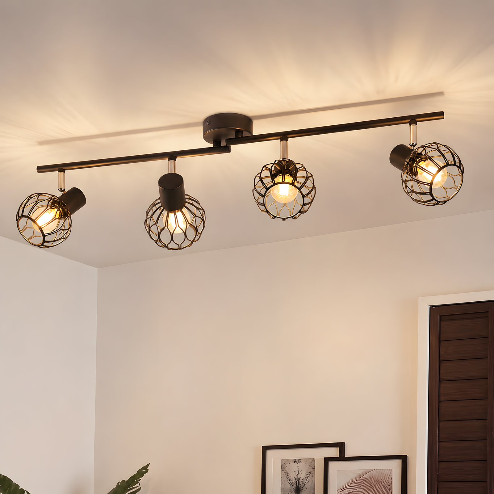 Un riel de iluminación negro con cuatro cabezales de foco ajustables, cada uno con diseño de jaula abierta y bombillas cálidas visibles, ilumina un techo blanco.