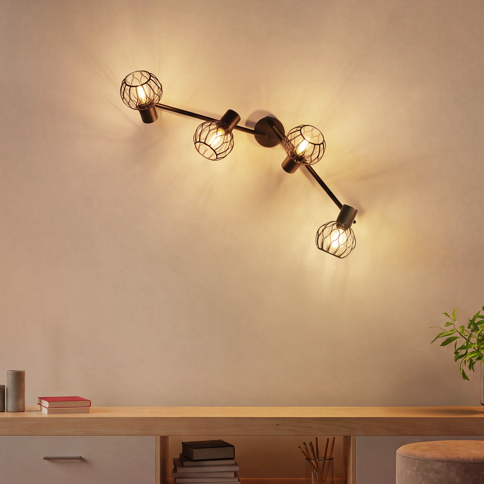 Eine schwarze Stromschienenleuchte mit vier korbförmigen Glühbirnen beleuchtet eine beige Wand.